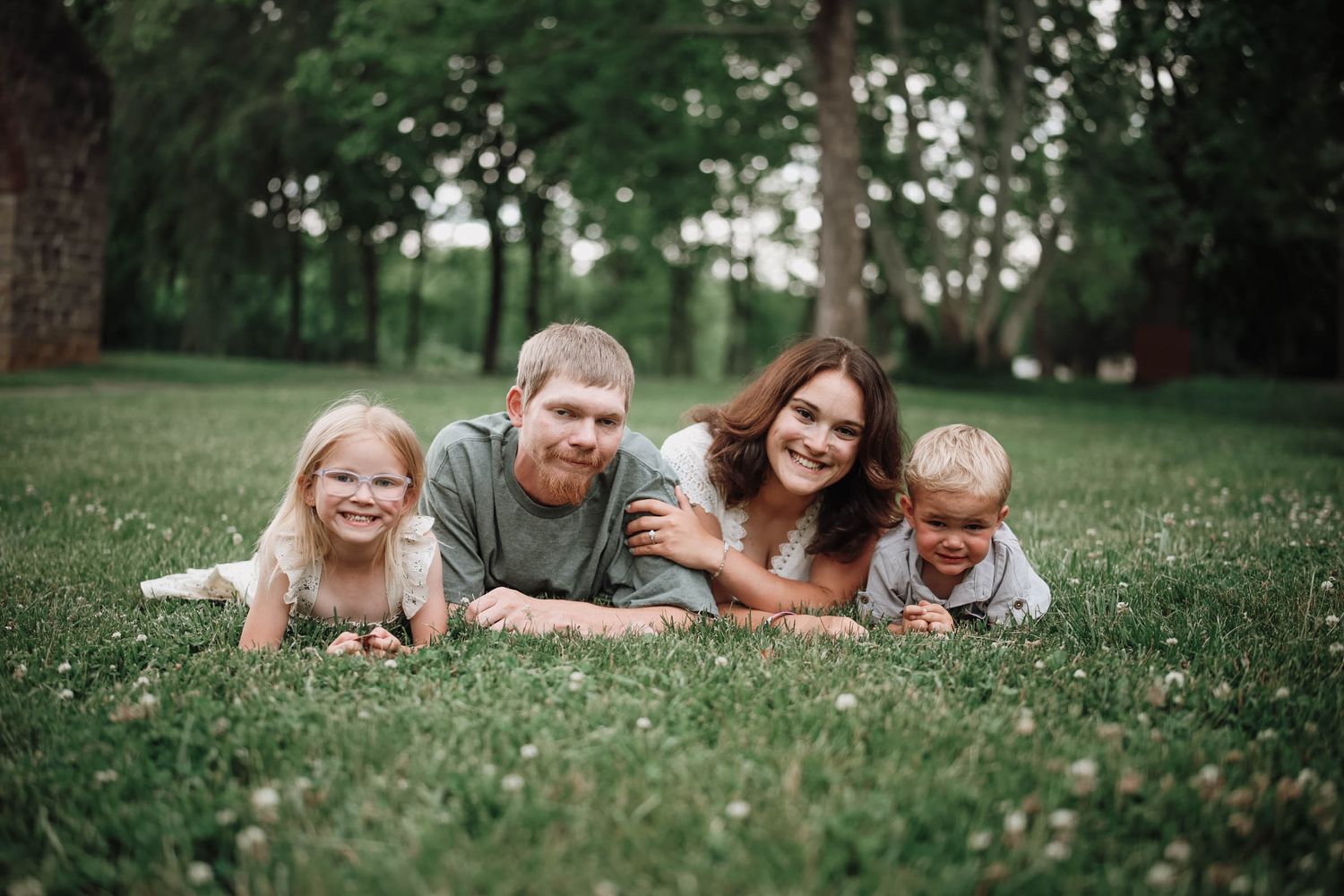 Happy family of four lying on green grass in a park, smiling at the camera.