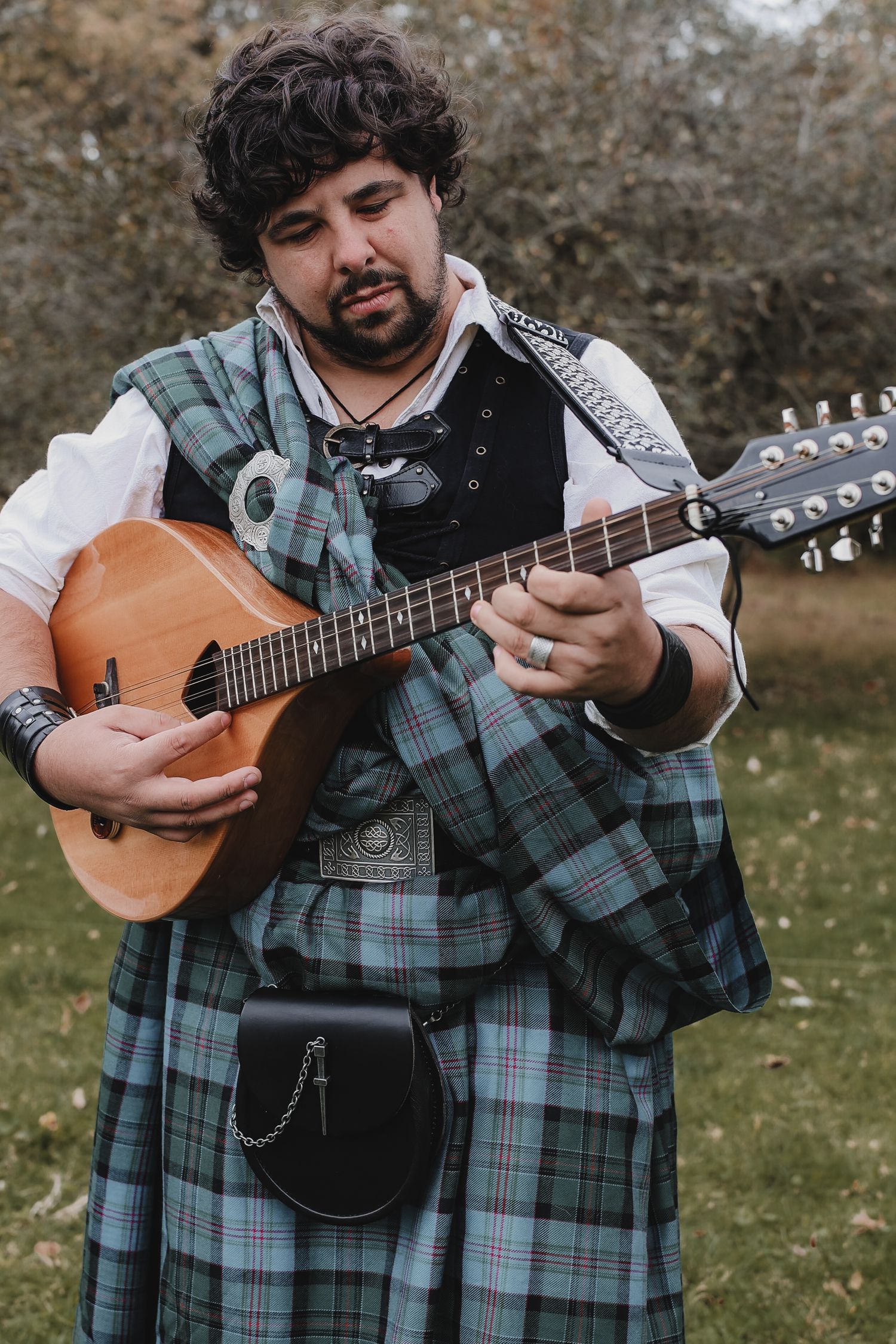 A musician in plaid kilt attire plays an acoustic guitar outdoors in a series of detailed close-up shots.