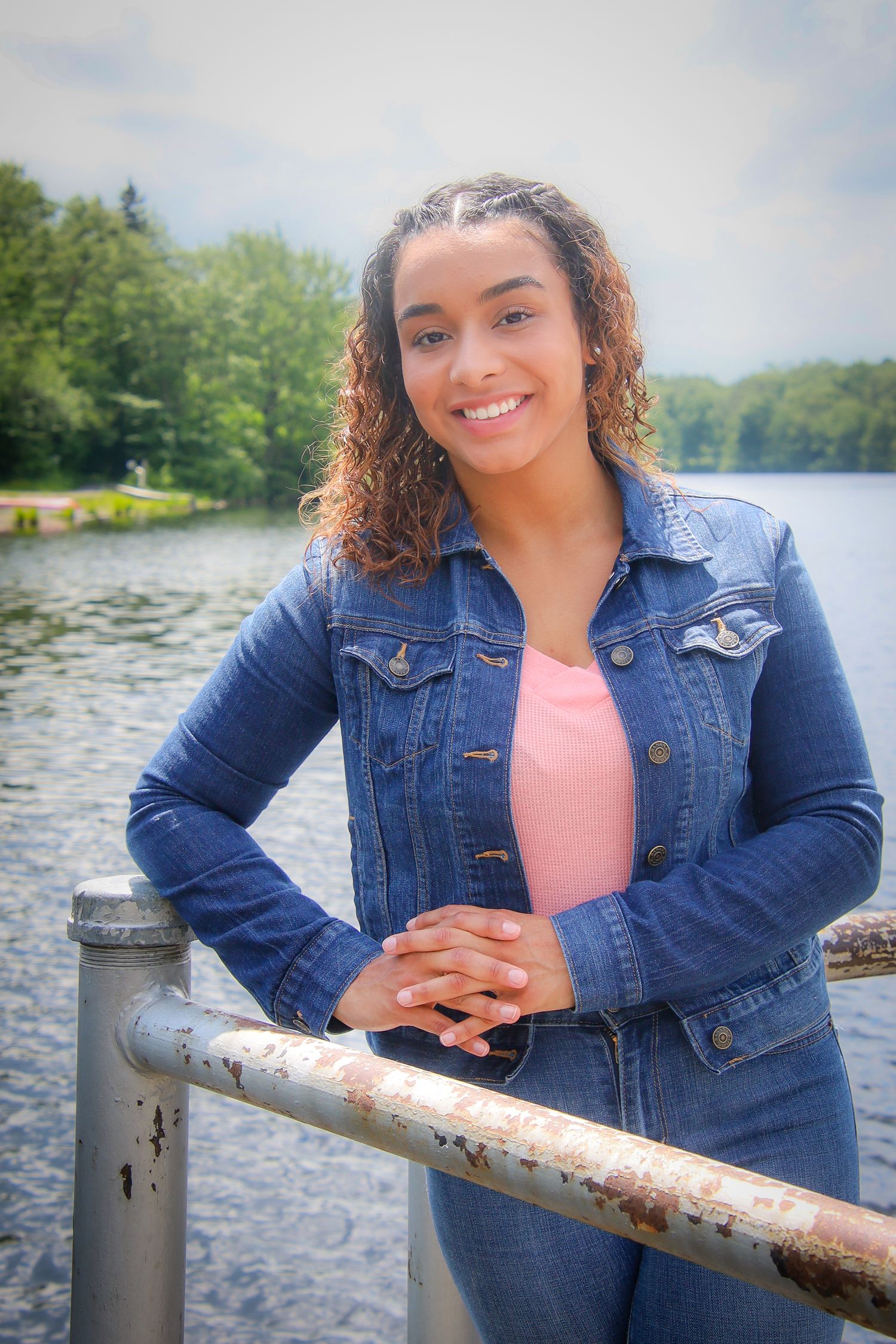 A series of outdoor photos by a lake showing someone in a denim jacket and coral top posing against a railing.