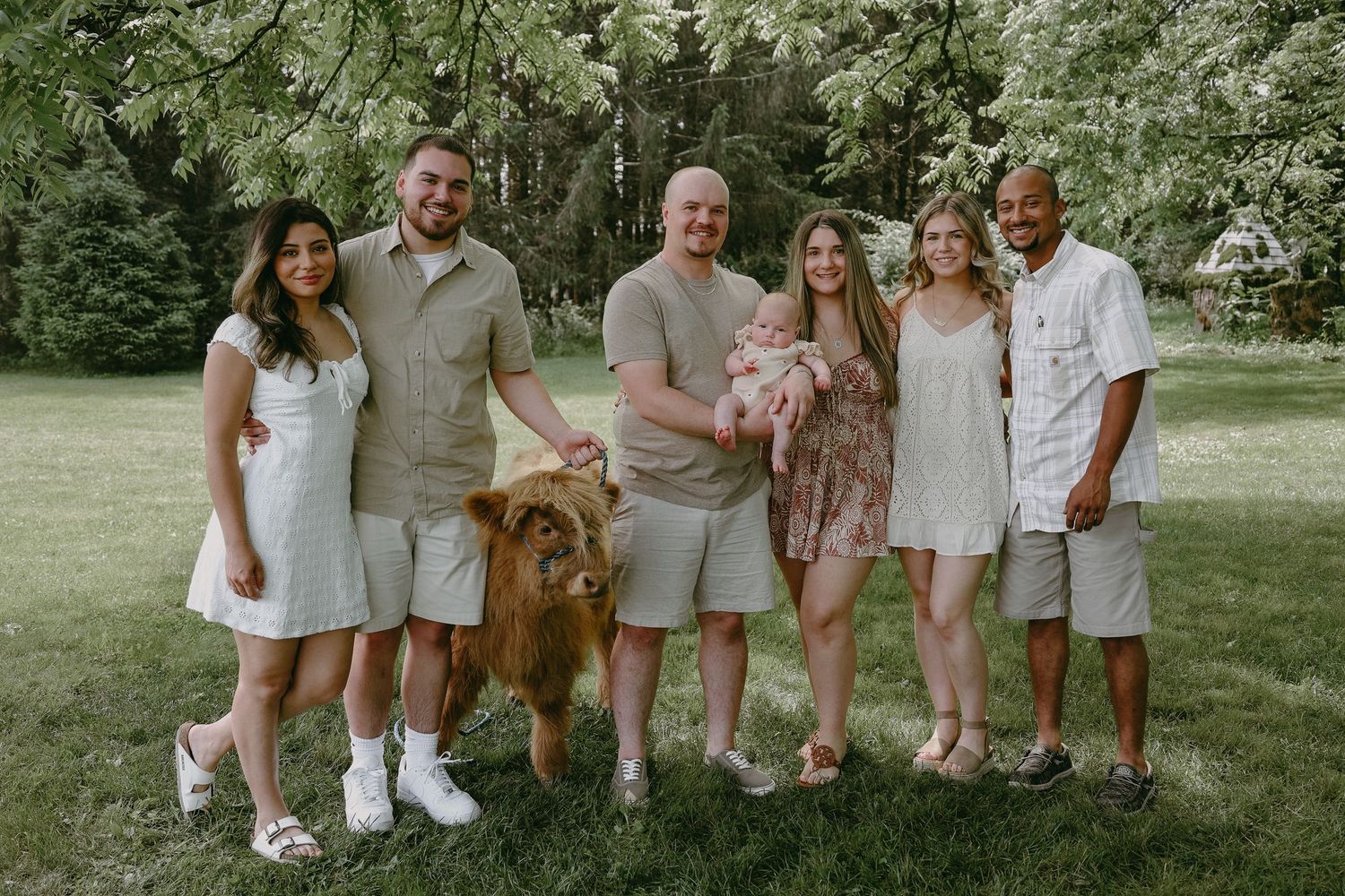 A group in coordinated light-colored outfits poses outdoors on grass with their golden retriever dog.