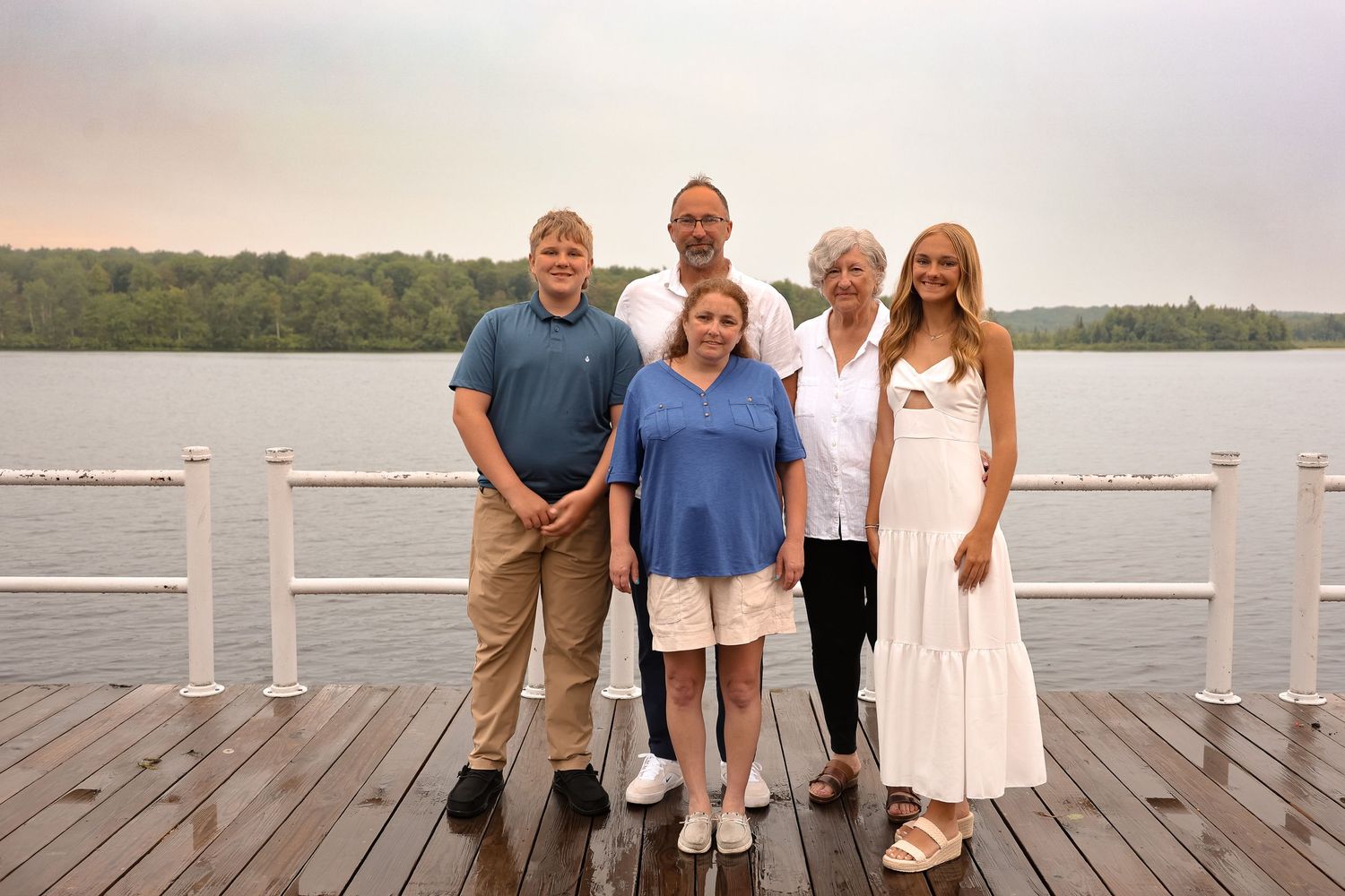 Family posing together with smiles on a wooden dock overlooking a peaceful lake during a sunny evening.