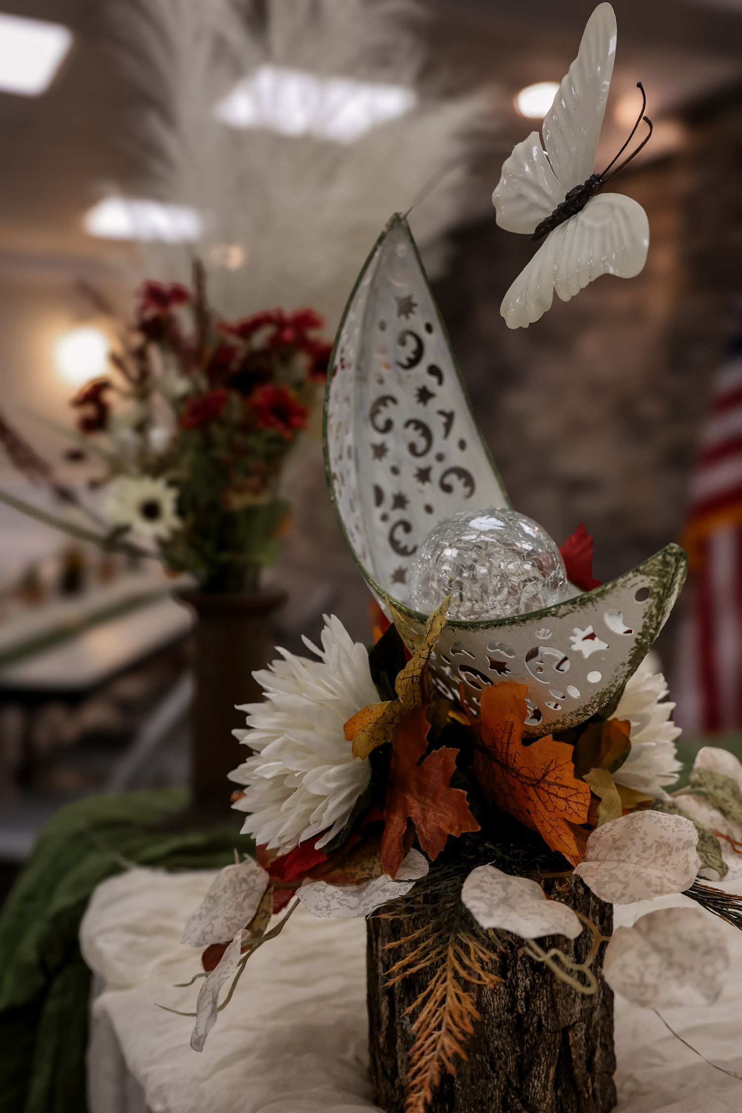 Decorative white butterflies and flowers arranged with autumn leaves in a rustic woodland centerpiece display.