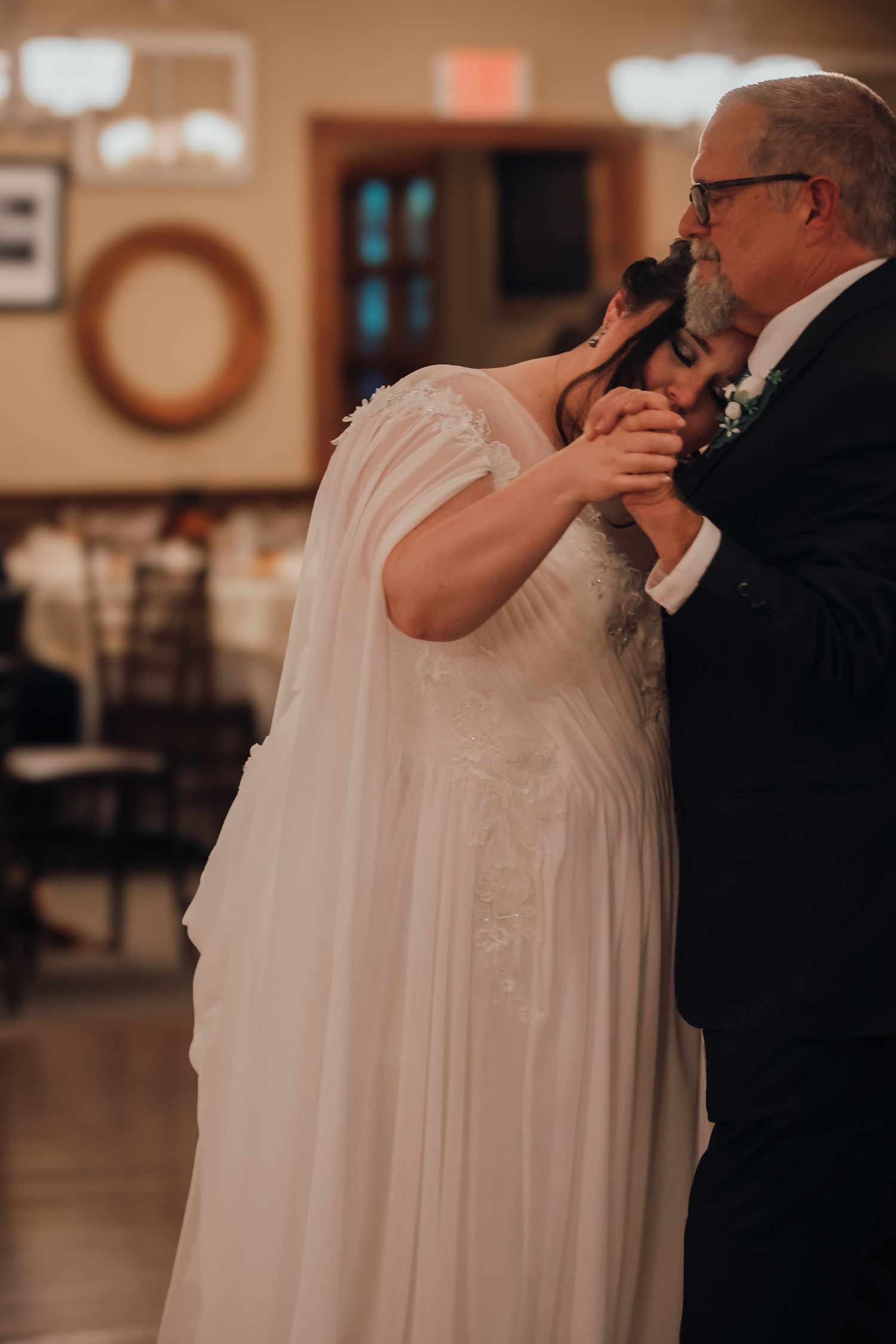A couple shares an intimate dance moment at a wedding reception in a warmly lit indoor venue.