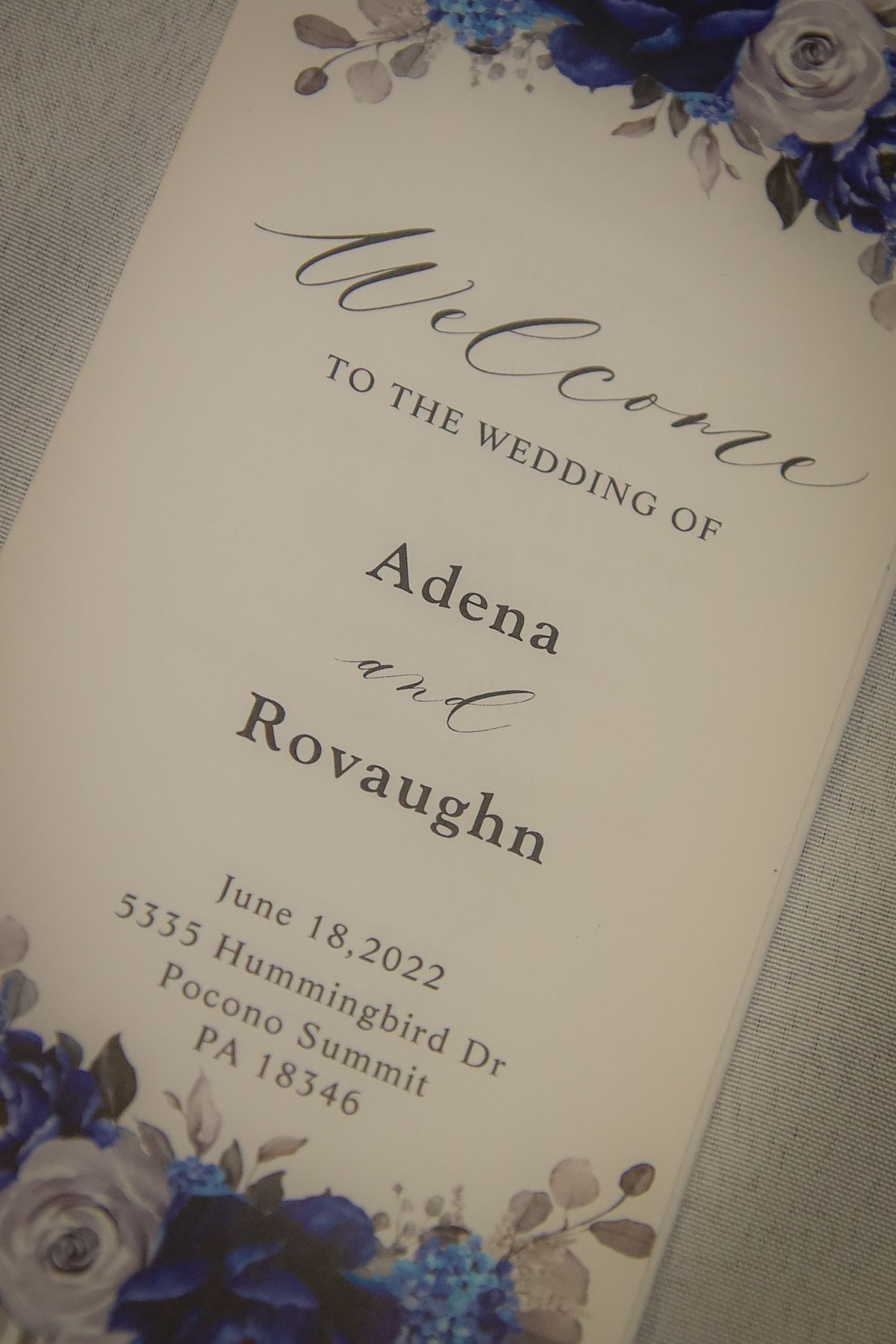Wedding invitation details showing elegant text and floral decorations in blue and gray tones on cream colored paper.