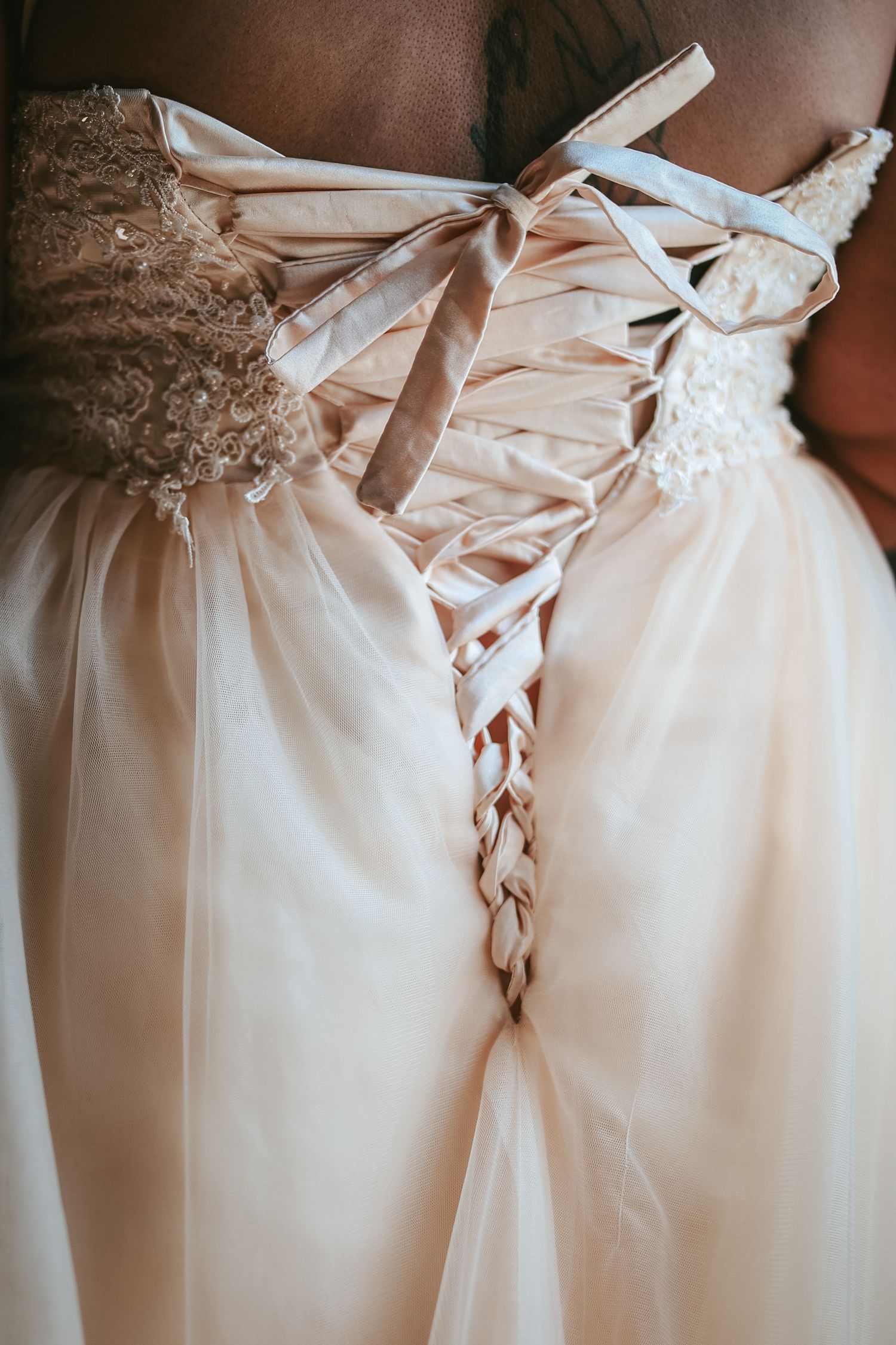 Close-up details of a wedding dress showing delicate lace-up corset back with satin ribbons and tulle fabric.