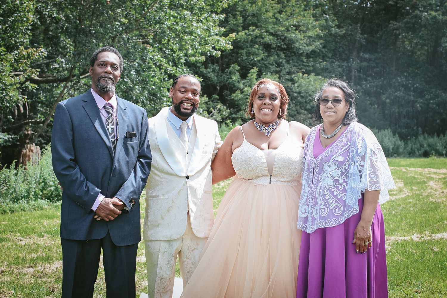 A group of people in formal attire gather outdoors for photos in a lush green garden setting.