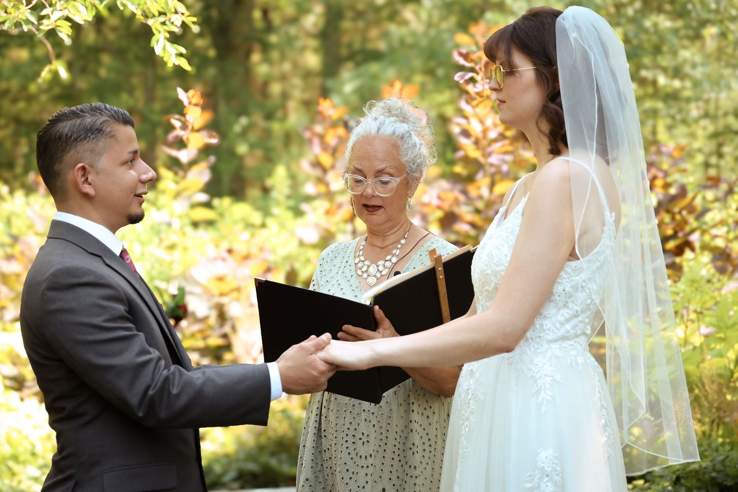 A wedding couple shares an intimate moment while dancing together in a sunlit wooded outdoor setting.