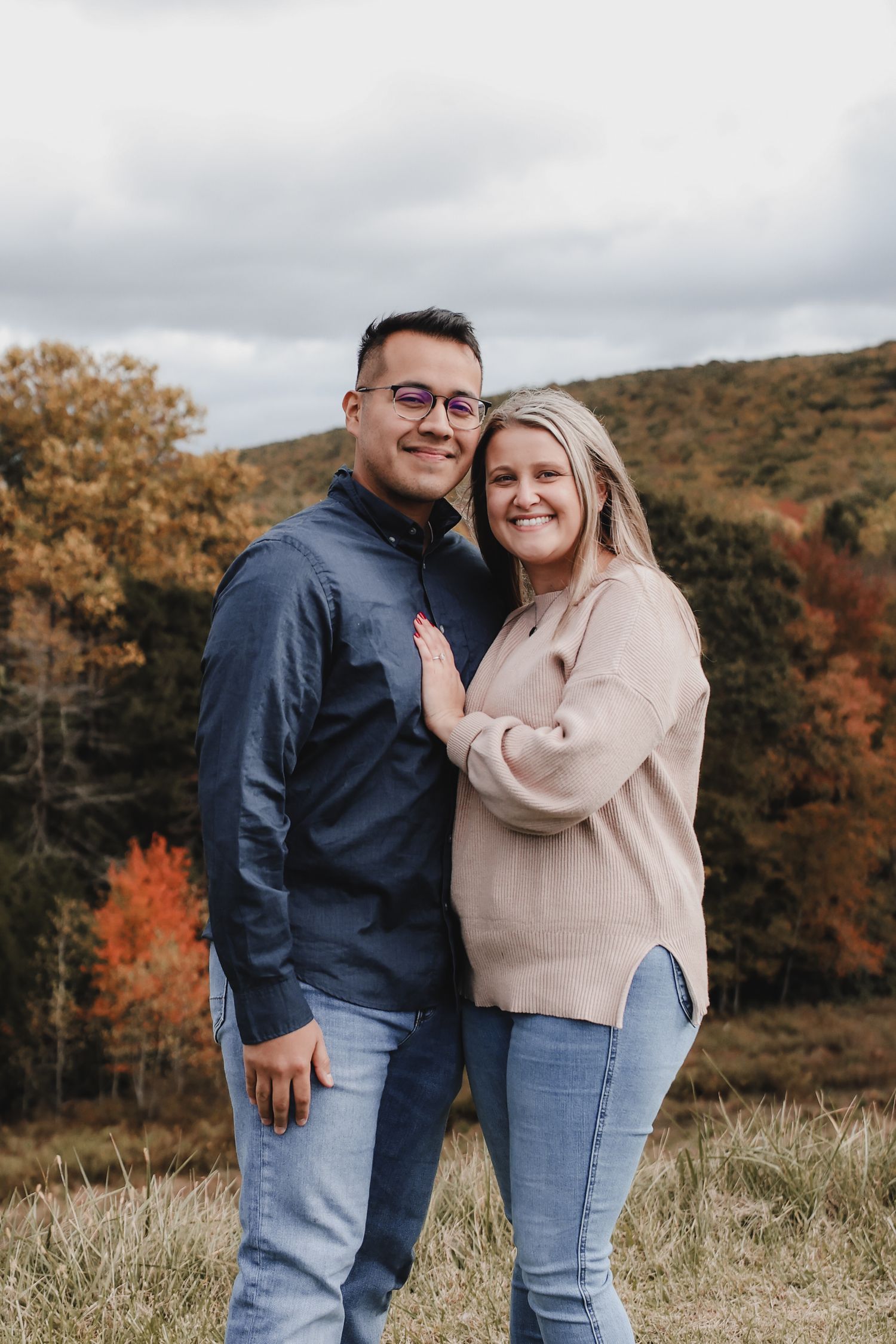 A couple shares joyful moments together against a backdrop of autumn foliage and rolling hills during a photo session.