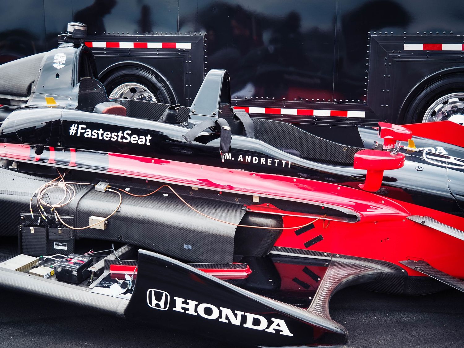 Close-up view of red and black Honda racing car components and bodywork at a motorsport event.