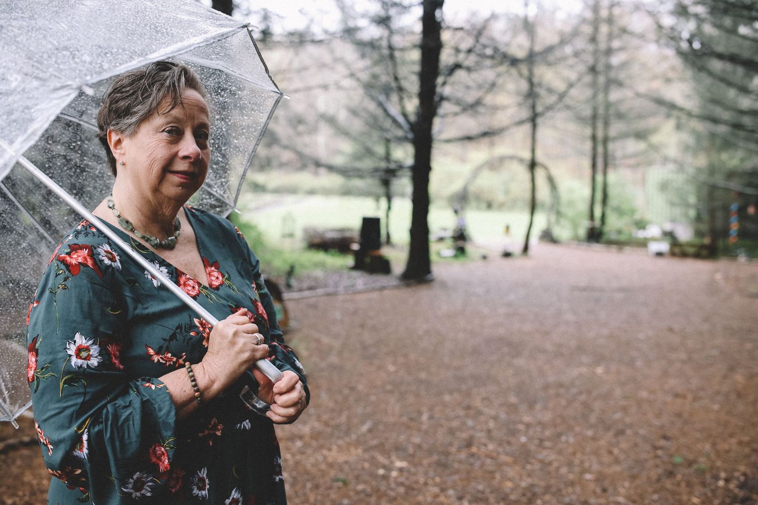 Person in teal jacket enjoying a peaceful moment in a forest setting surrounded by autumn leaves and trees.
