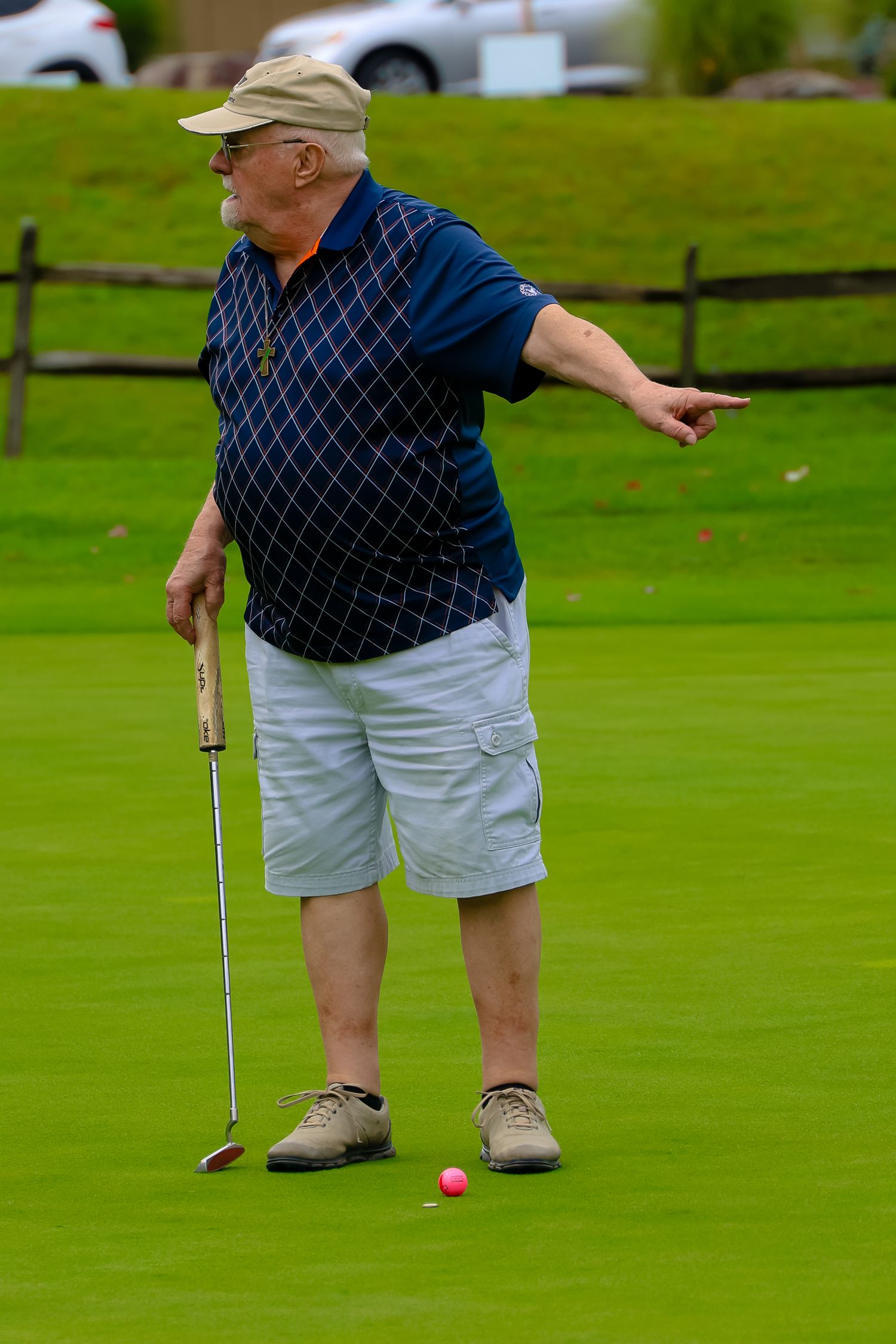 Golfer in navy sweater and khaki shorts lines up a putt on a lush green course.