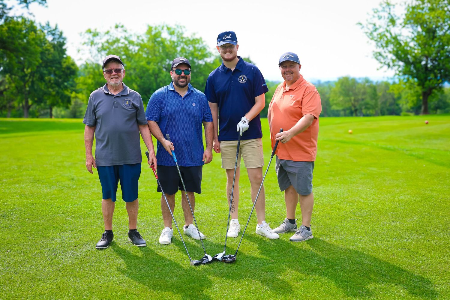 Group of golfers standing together on a lush green golf course during a sunny summer day.