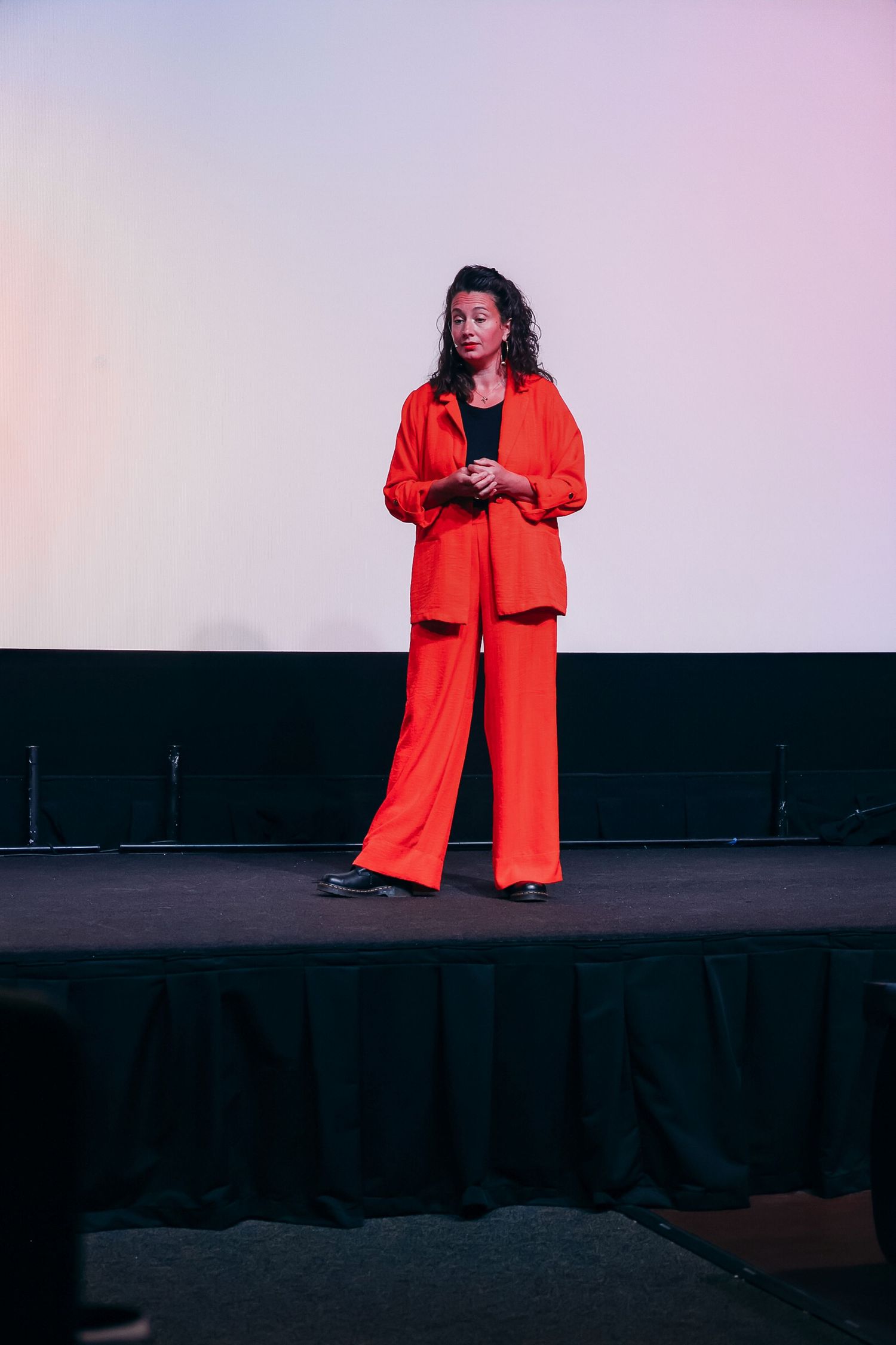 Woman in red pantsuit standing on stage during a presentation or speaking event.