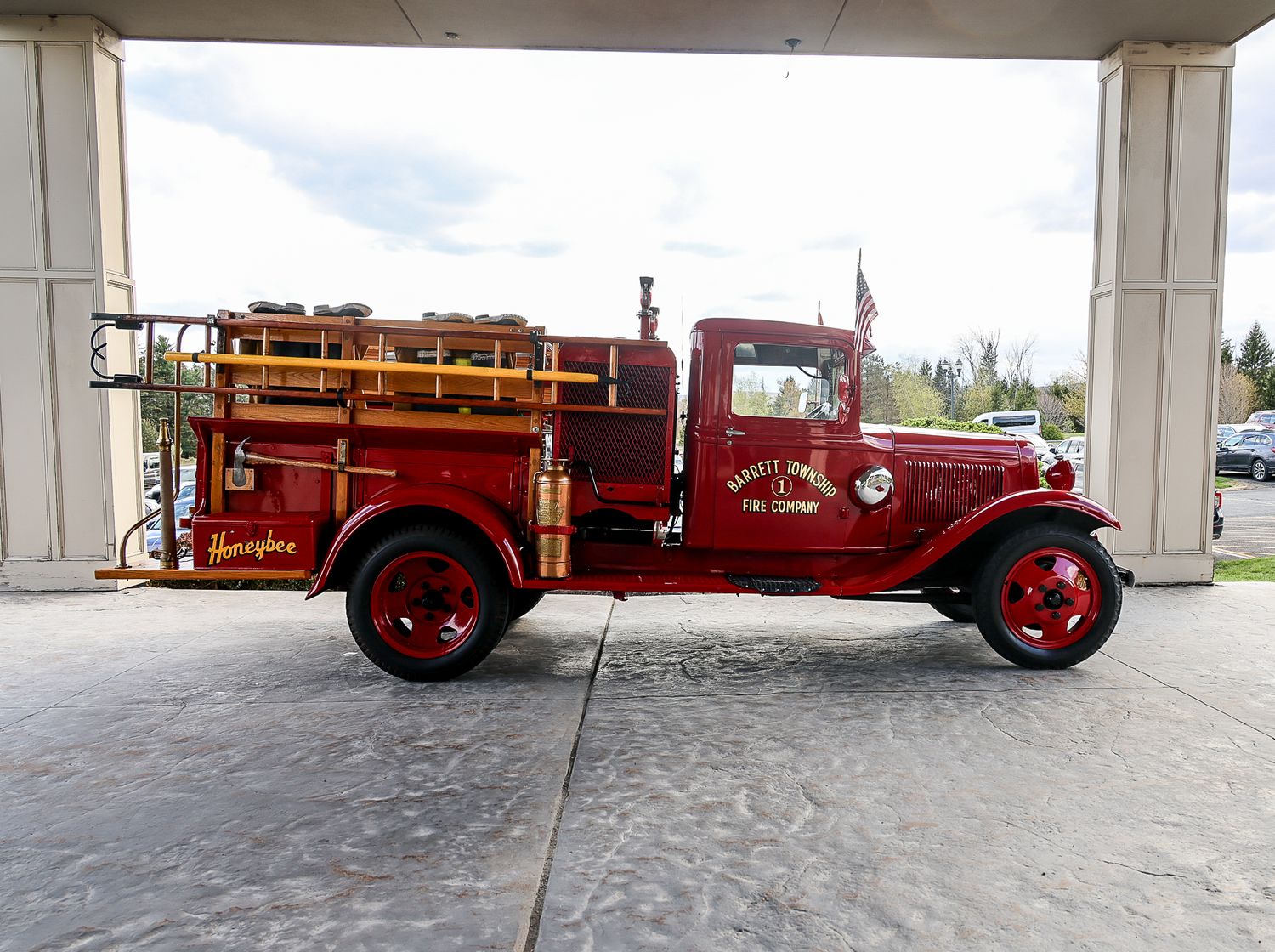 Vintage red antique fire truck parked under a covered area, featuring wooden ladders and classic early 20th century design.