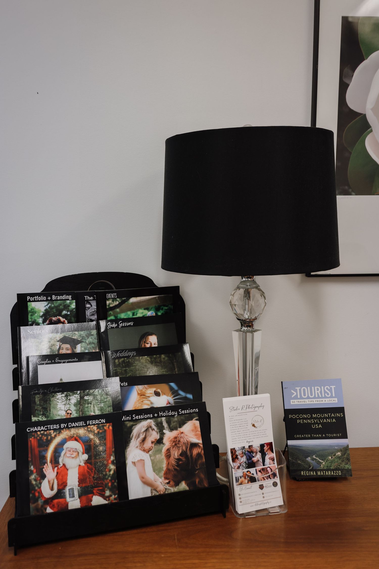 A row of black table lamps with photo frames displayed underneath on a wooden surface against a white wall.