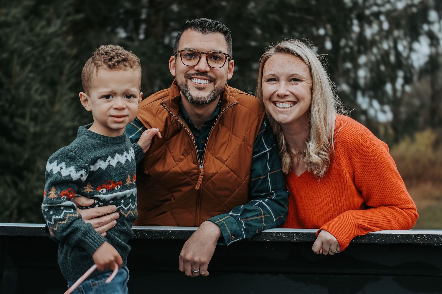 A family poses together outdoors during an autumn photo session wearing coordinated orange and brown outfits.