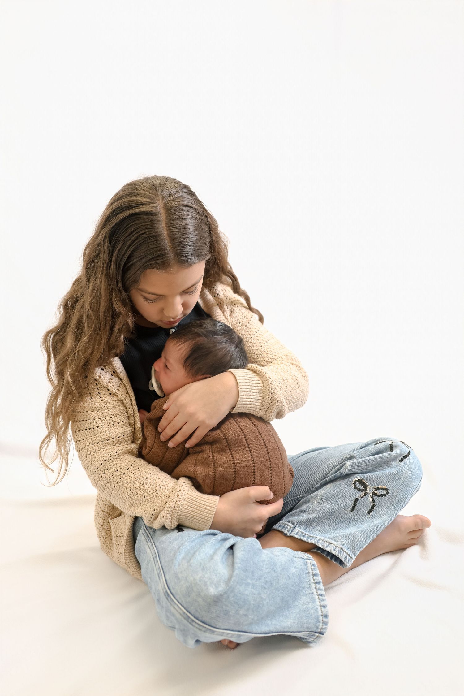 Person wearing beige sweater and jeans curled up on white floor in three emotional poses.