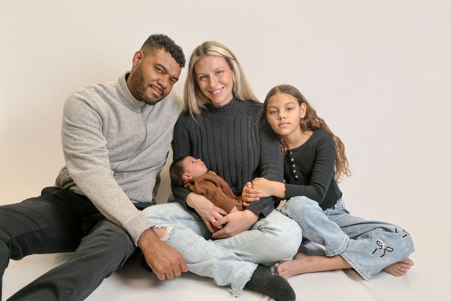 A family relaxes together in casual outfits while lying on a light colored background for a portrait session.