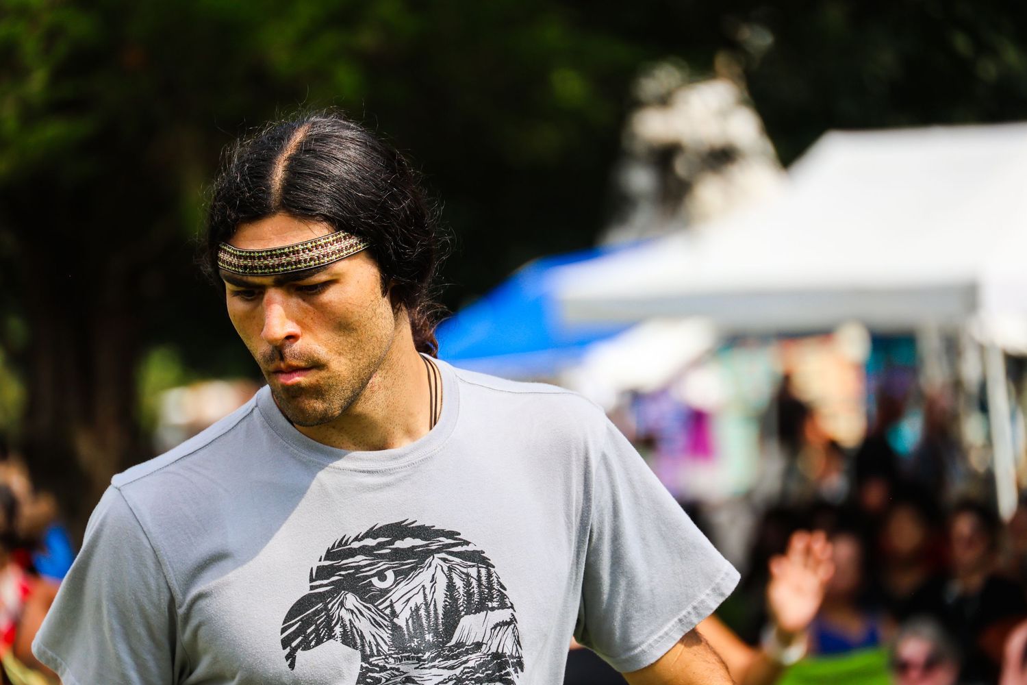A person wearing a gray t-shirt with a graphic design stands outdoors at a crowded event.
