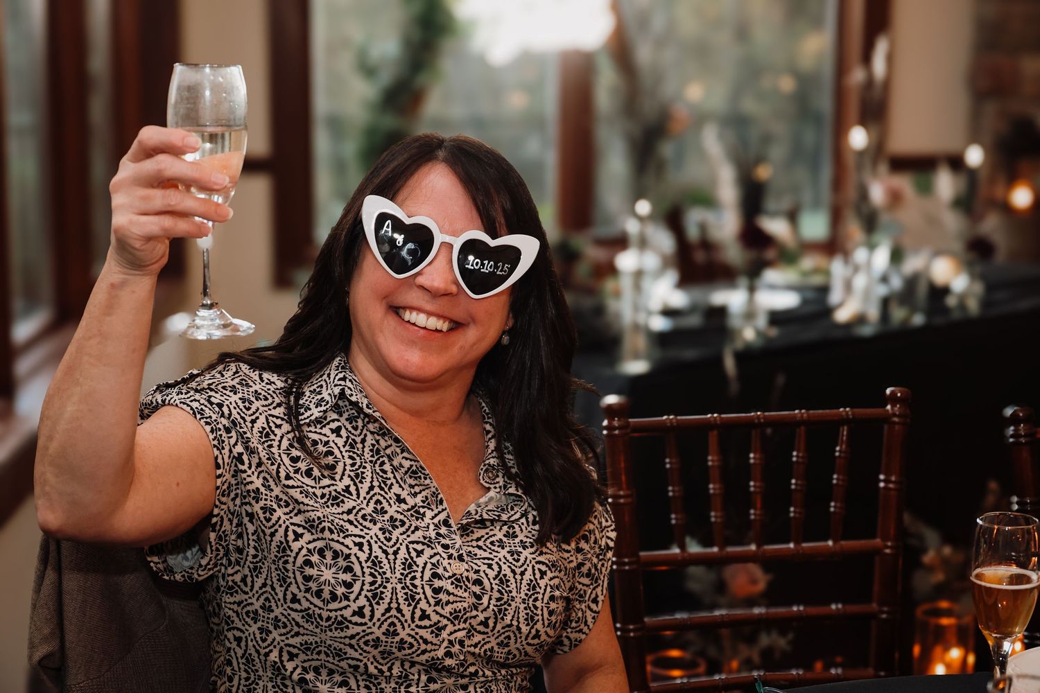 Someone wearing a black and white patterned dress raises a wine glass in celebration at a restaurant.