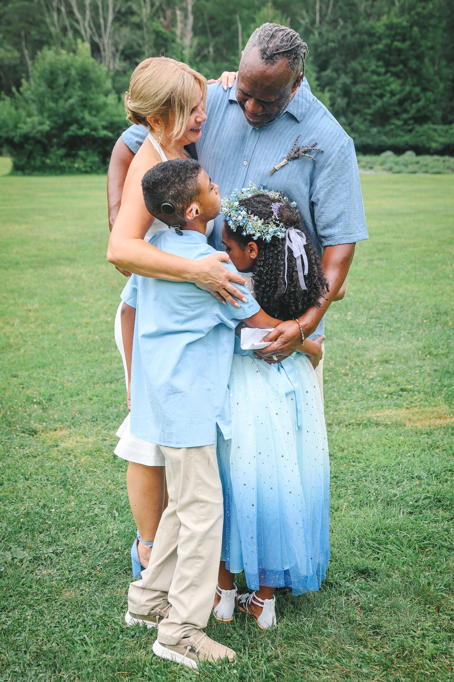 Family members share tender embraces in a grassy outdoor setting wearing coordinated blue and white outfits.