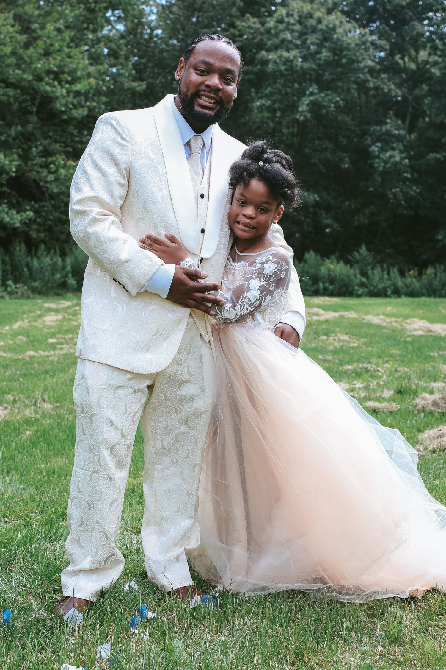 A couple in wedding attire shares joyful moments together outdoors in a grassy setting.