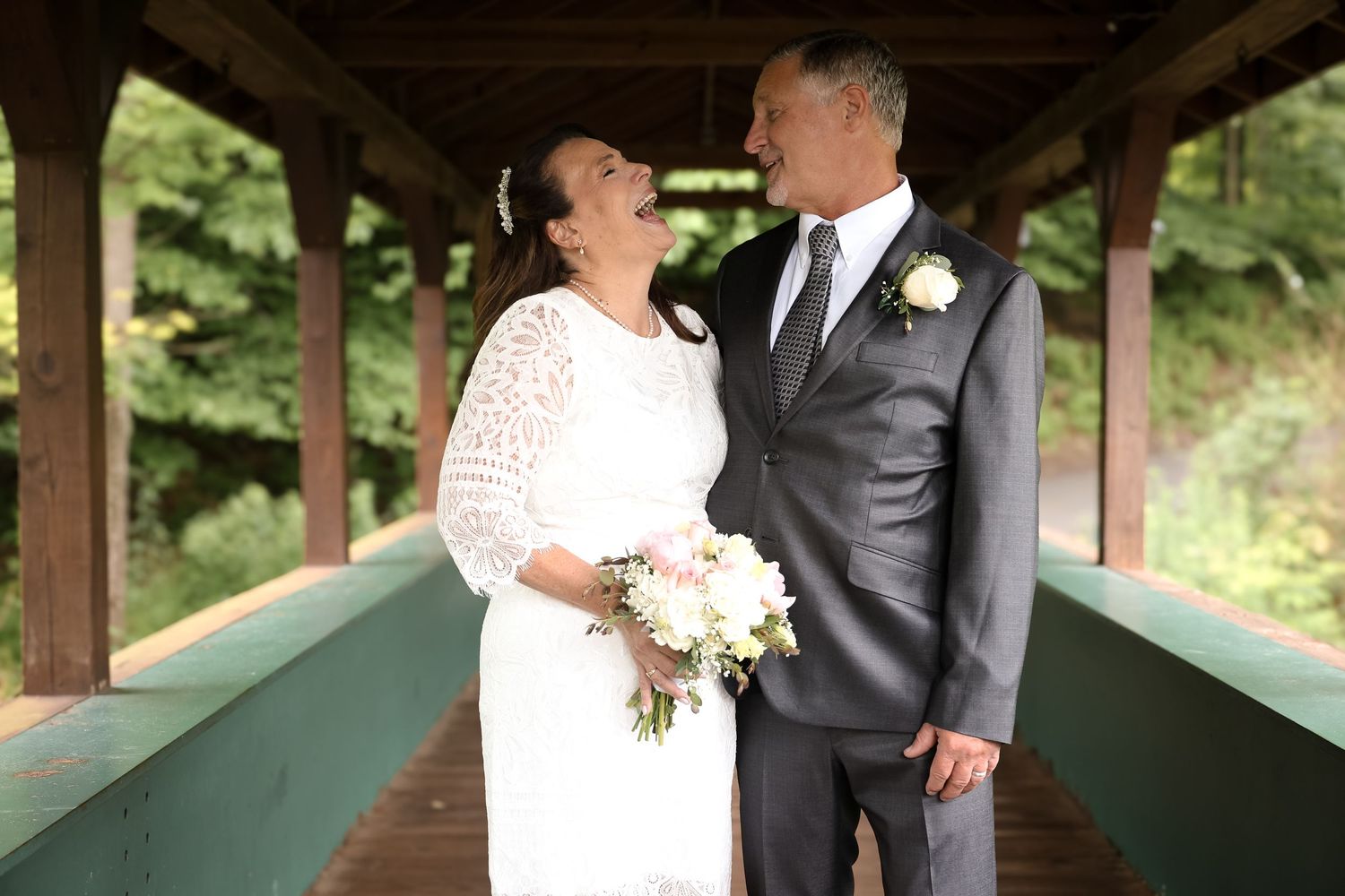 Couple sharing a joyful moment under a wooden gazebo during their outdoor wedding celebration.
