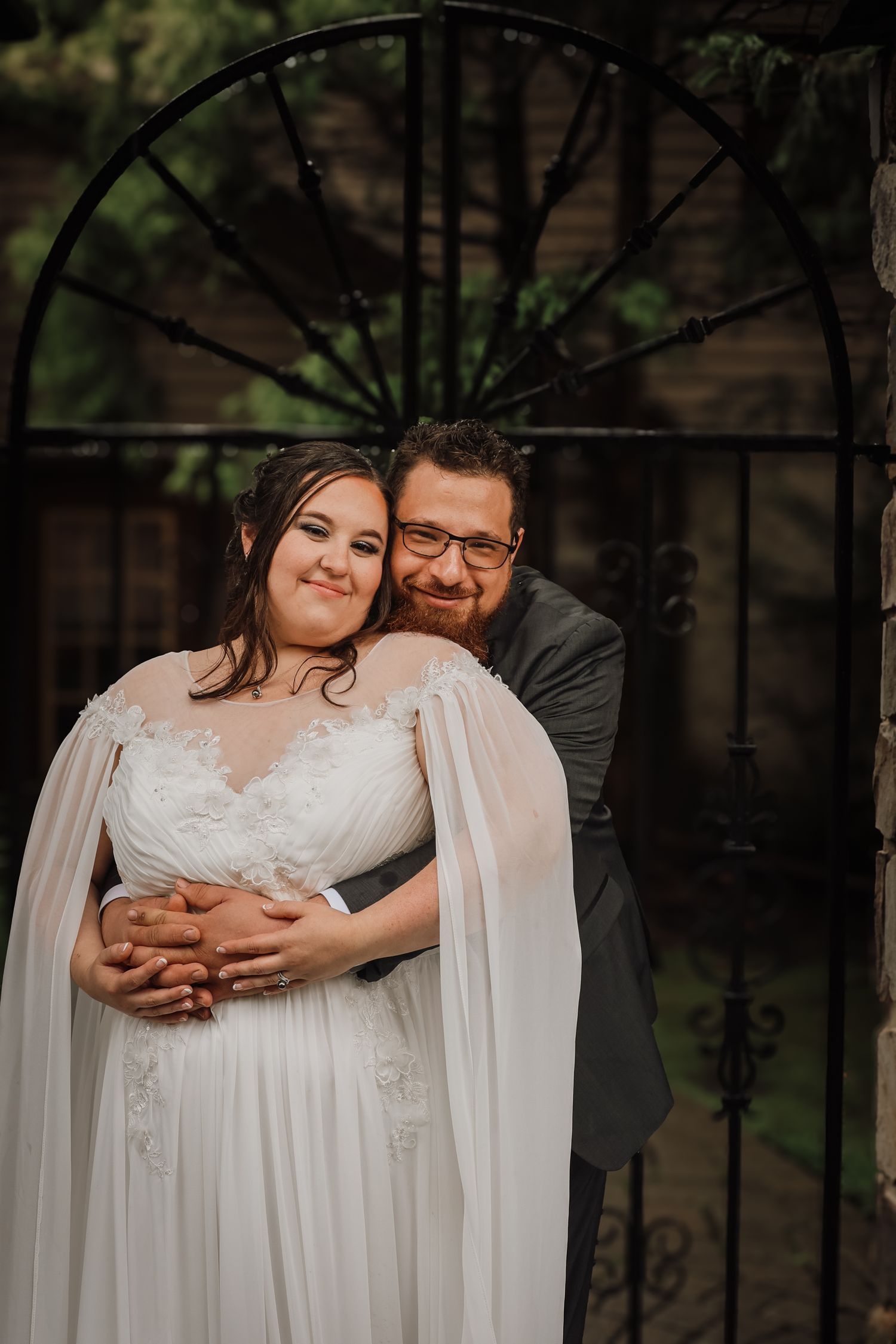 Romantic wedding couple embraces in a dreamy outdoor setting with flowing white dress and dark background.