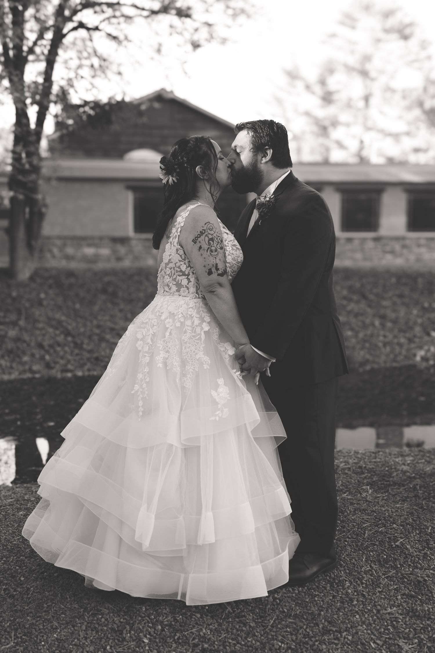 A couple in wedding attire shares intimate moments in a series of black and white outdoor portraits on a lawn.