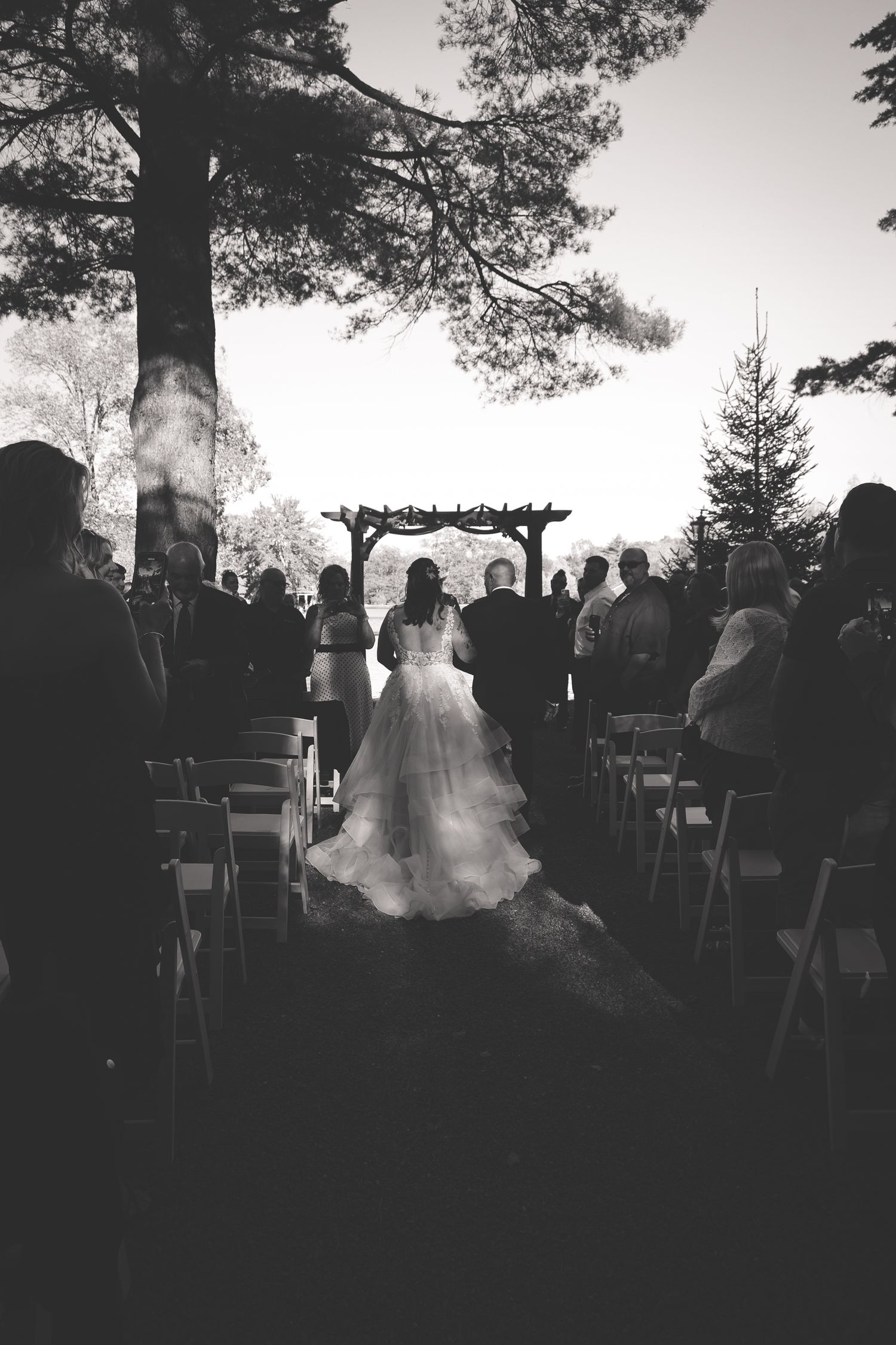 A series of black and white wedding ceremony photos showing silhouettes of guests gathered under trees at an outdoor venue.