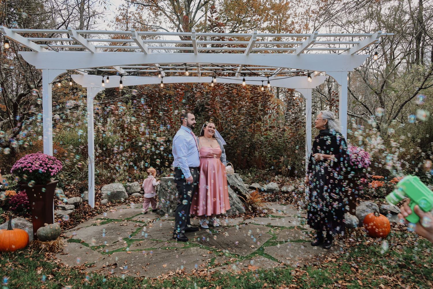 People gathered in a fall garden setting with autumn leaves and pumpkins during a festive outdoor celebration.