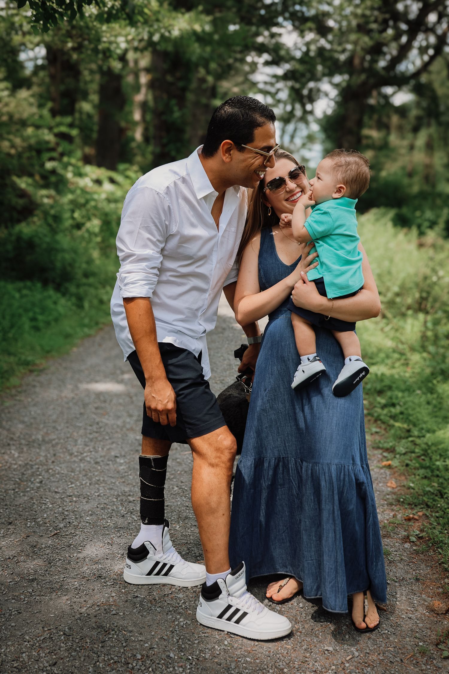 A family shares tender moments together on a wooded path, wearing casual attire and enjoying nature.