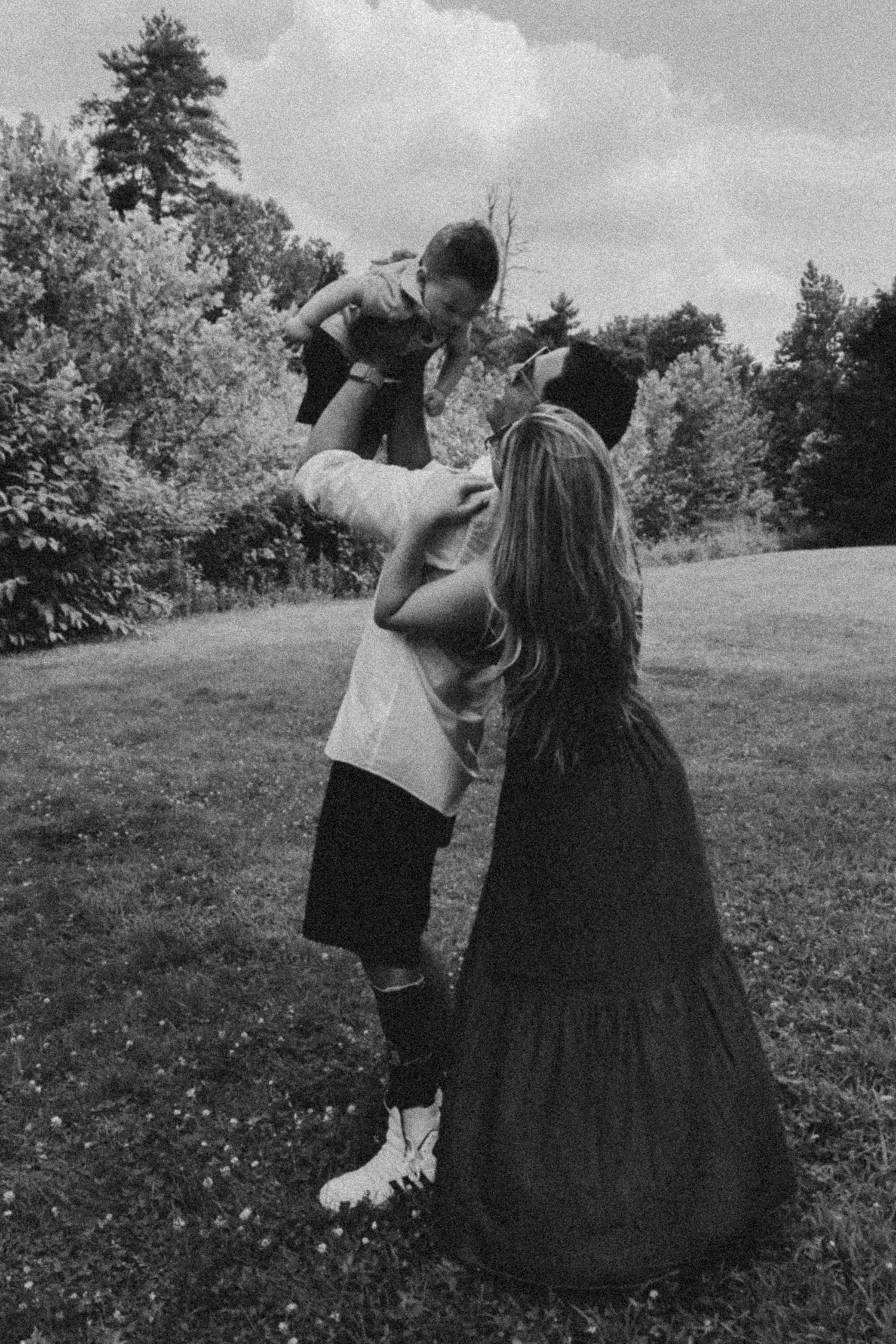 Two people in vintage clothing dance together in a grassy meadow with trees in the background.