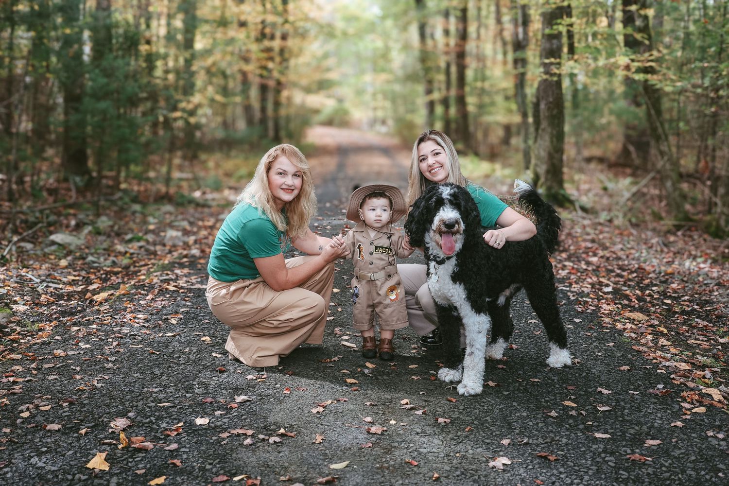 A group sits together on fallen autumn leaves in a wooded forest setting during a casual outdoor photoshoot.