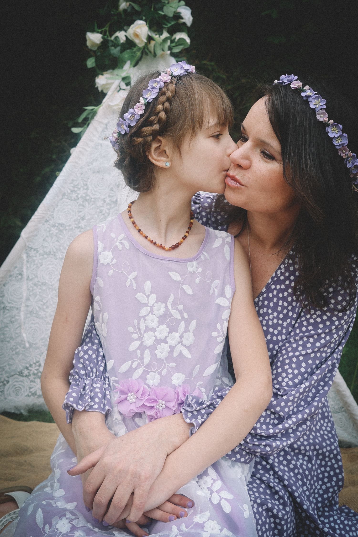 A tender moment captured outdoors showing affection between two people wearing purple and pink floral outfits.