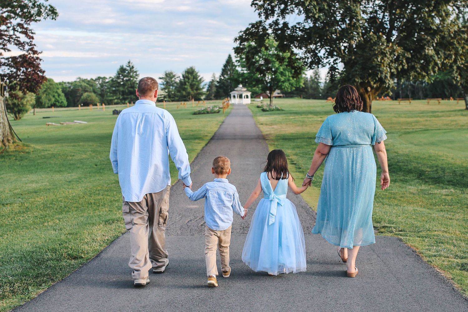 A group in coordinating blue and beige outfits walks together down a winding path through a grassy field.