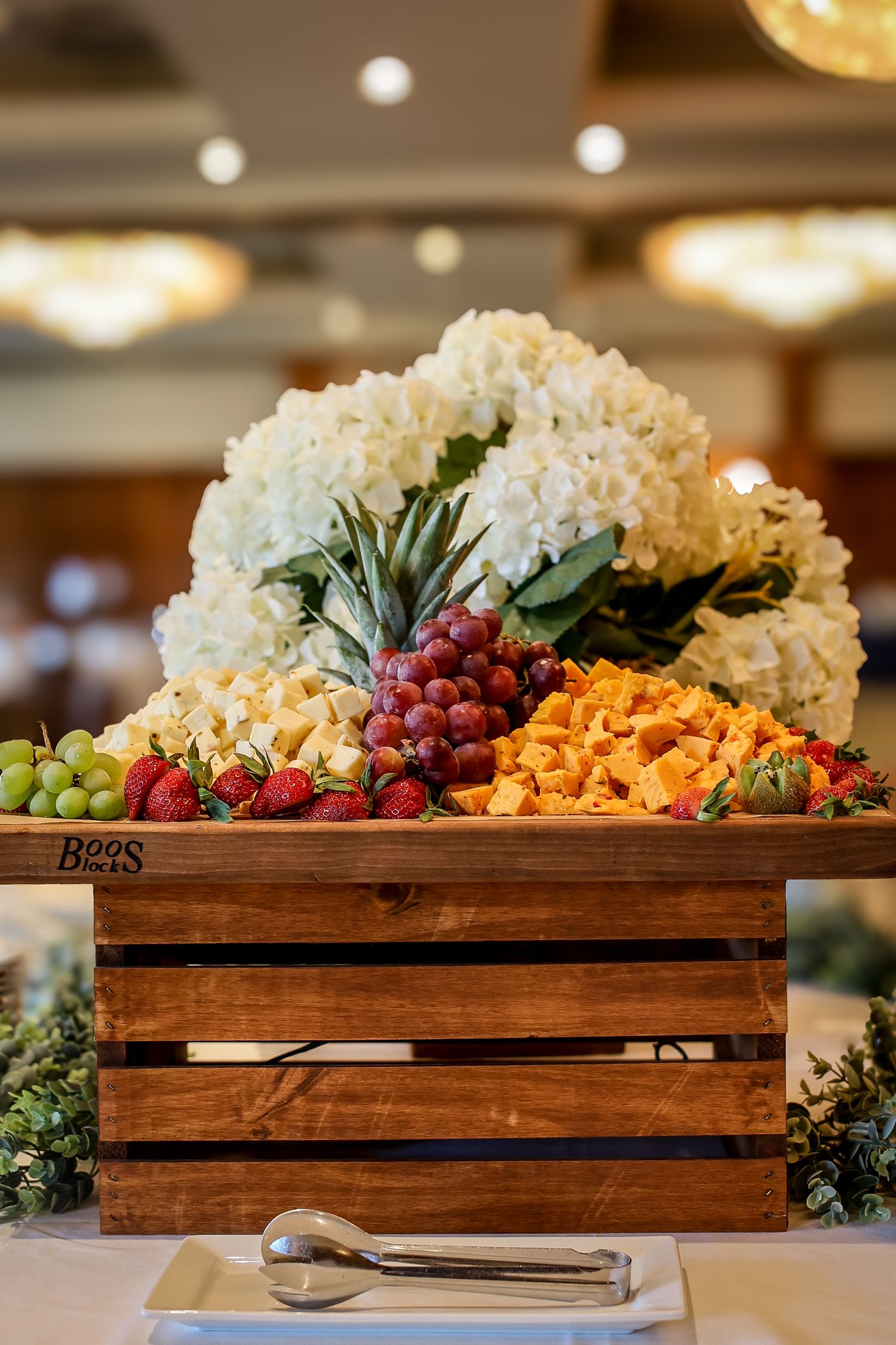 A rustic wooden crate filled with fresh fruits and white hydrangeas creates an elegant buffet display centerpiece.