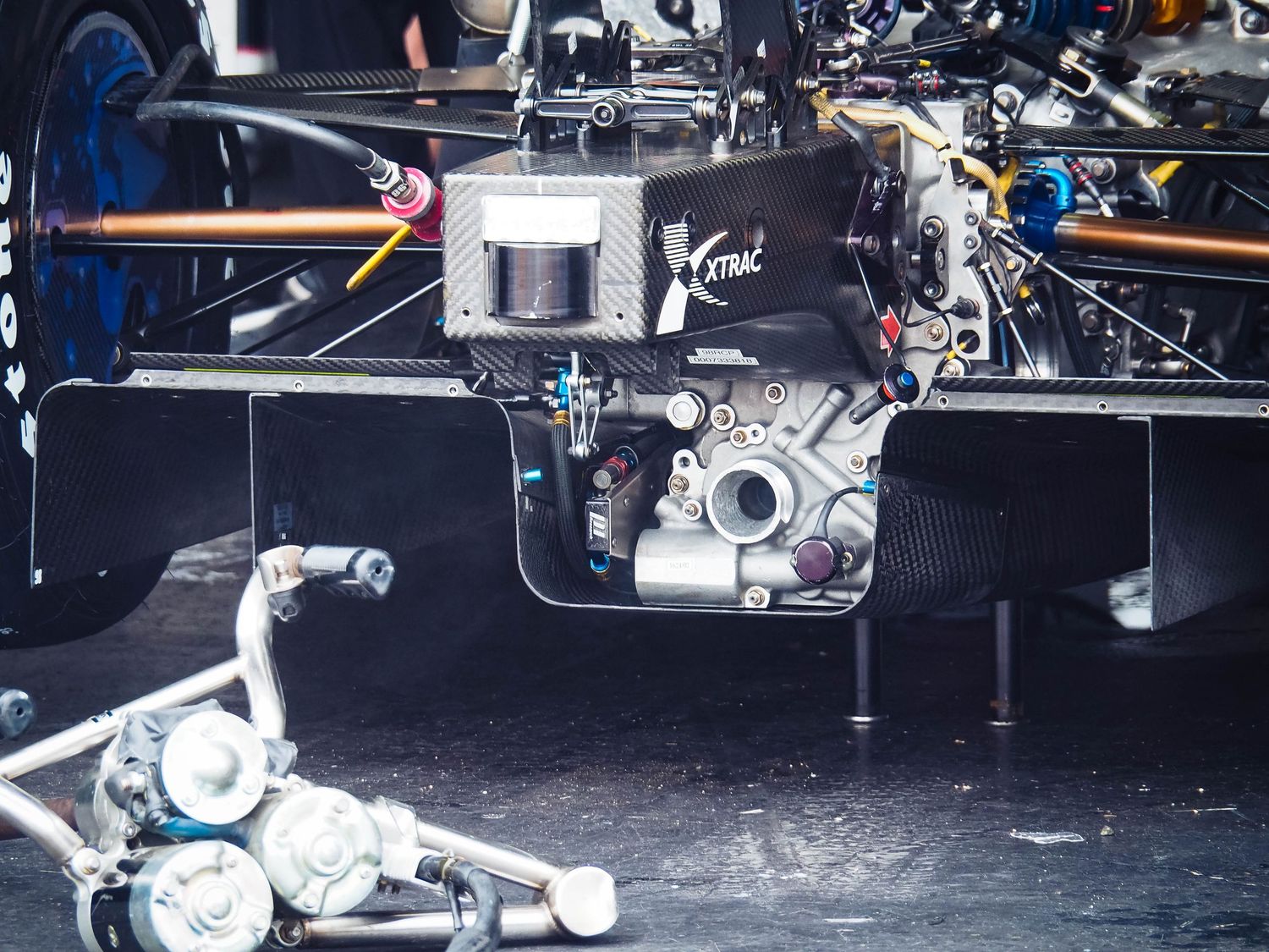 Close-up view of a racing car engine and mechanical components with exposed parts and tubing.
