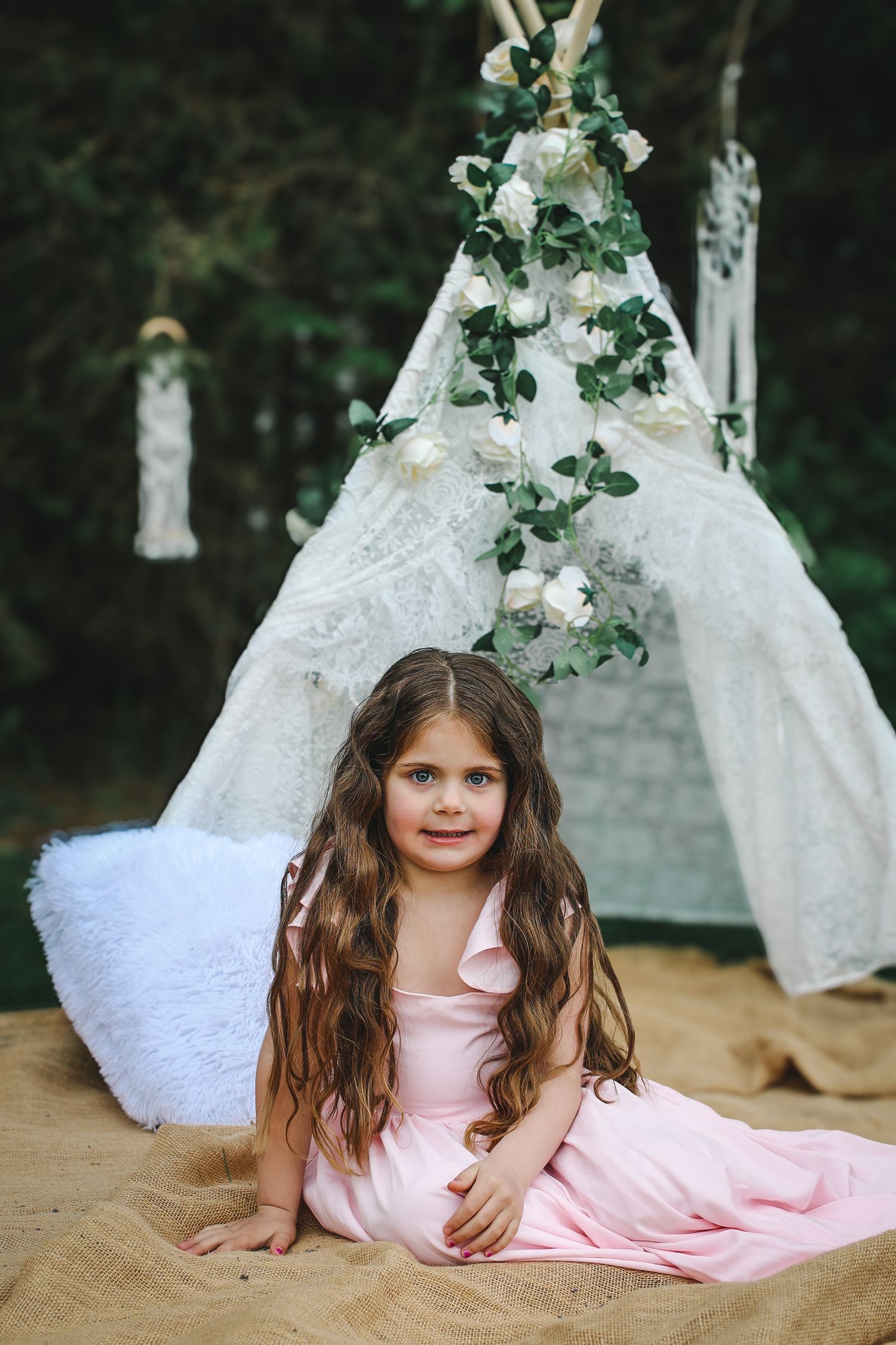 A decorative white lace teepee adorned with floral vines and greenery creates a whimsical outdoor setting.