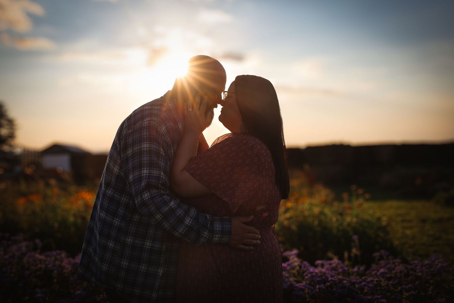 Silhouettes of a couple embracing in a golden sunset with wildflowers in the foreground.