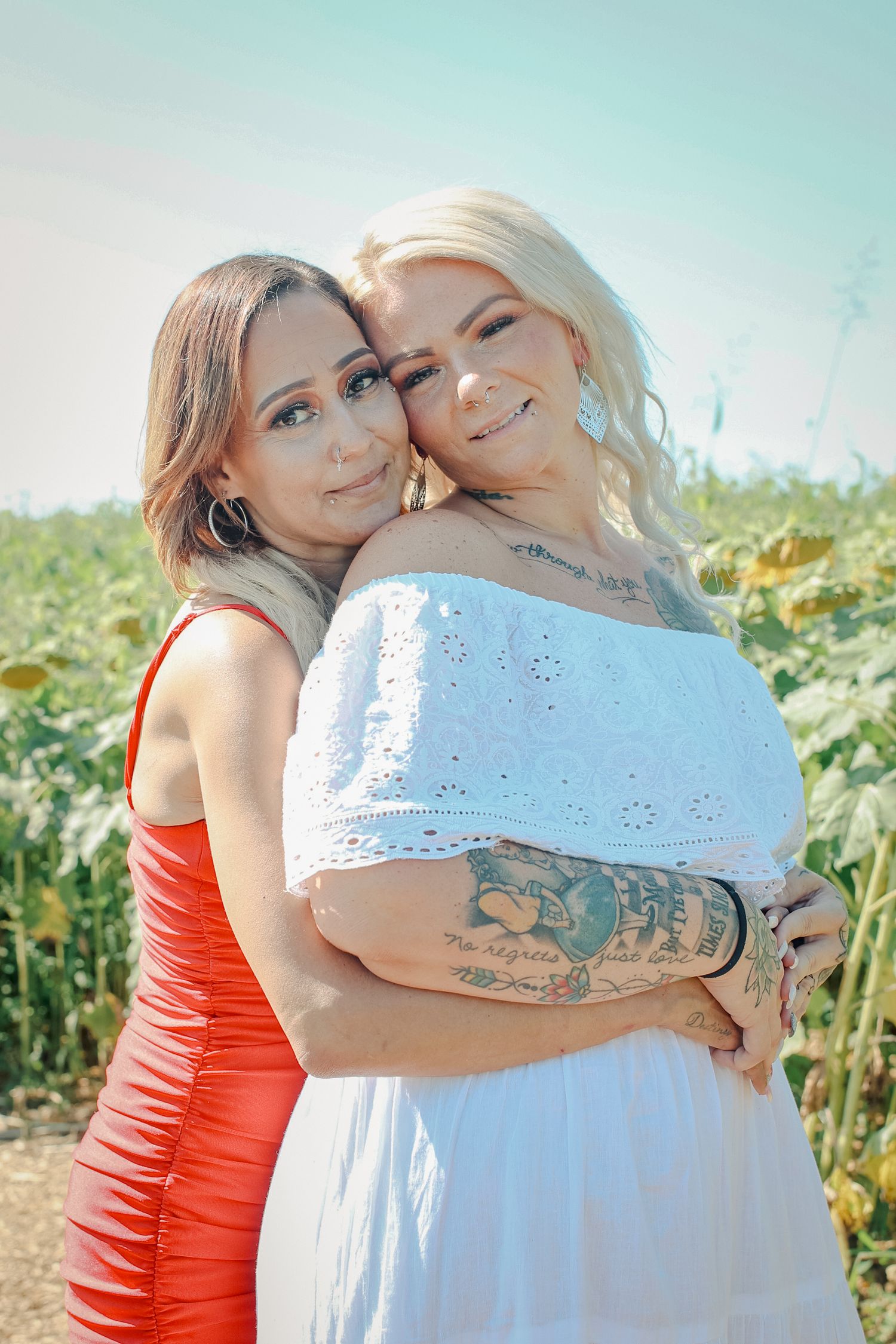 Two friends pose together outdoors in a field on a sunny day wearing red and white dresses.