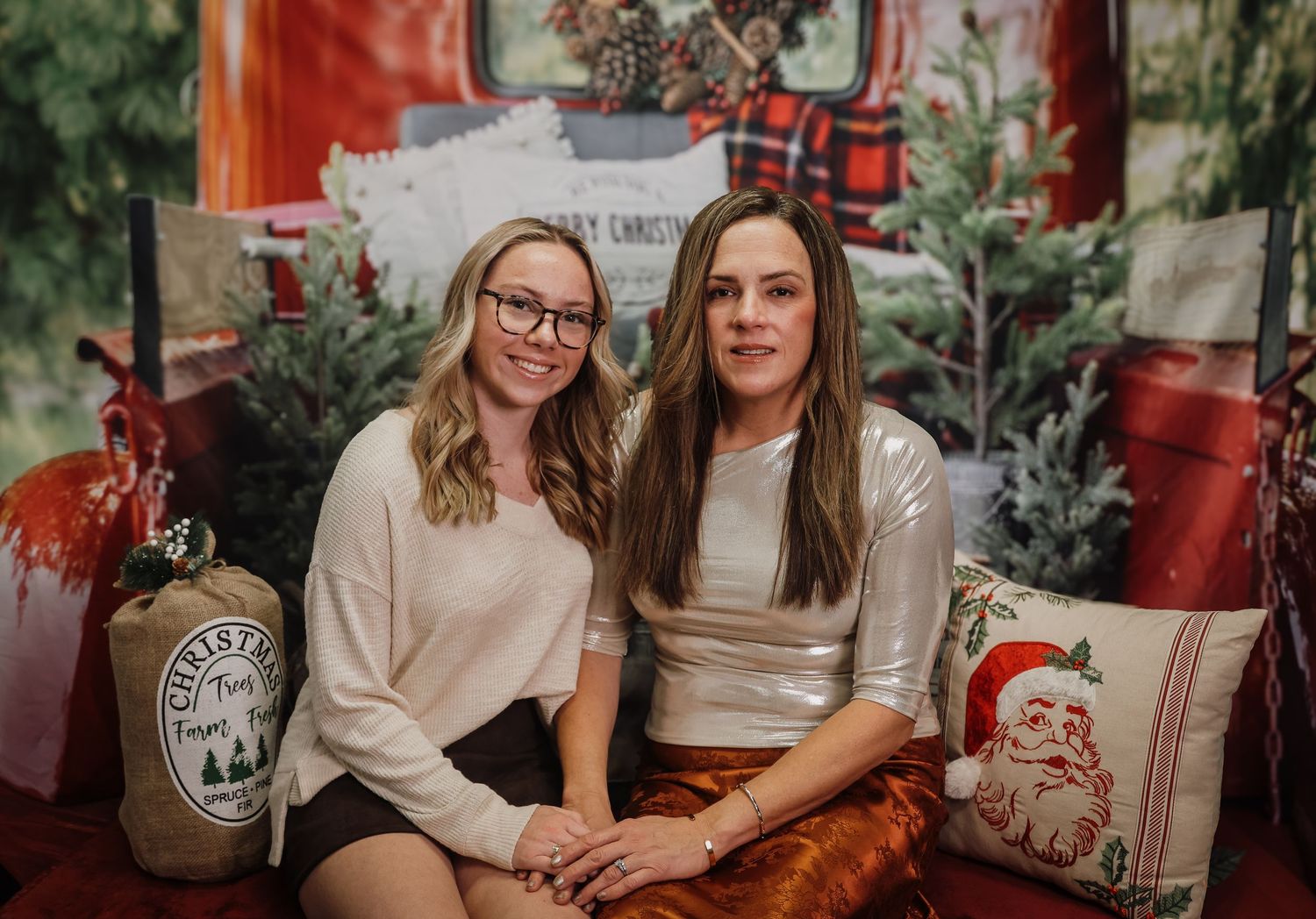 Two people sit close together on a couch in a cozy holiday setting with red plaid decor and greenery.
