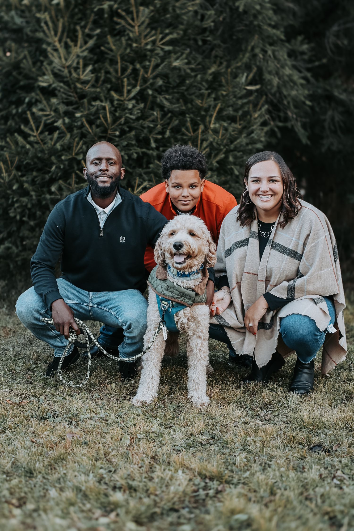 A group sits together on grass with a fluffy white dog, creating a casual outdoor portrait scene.