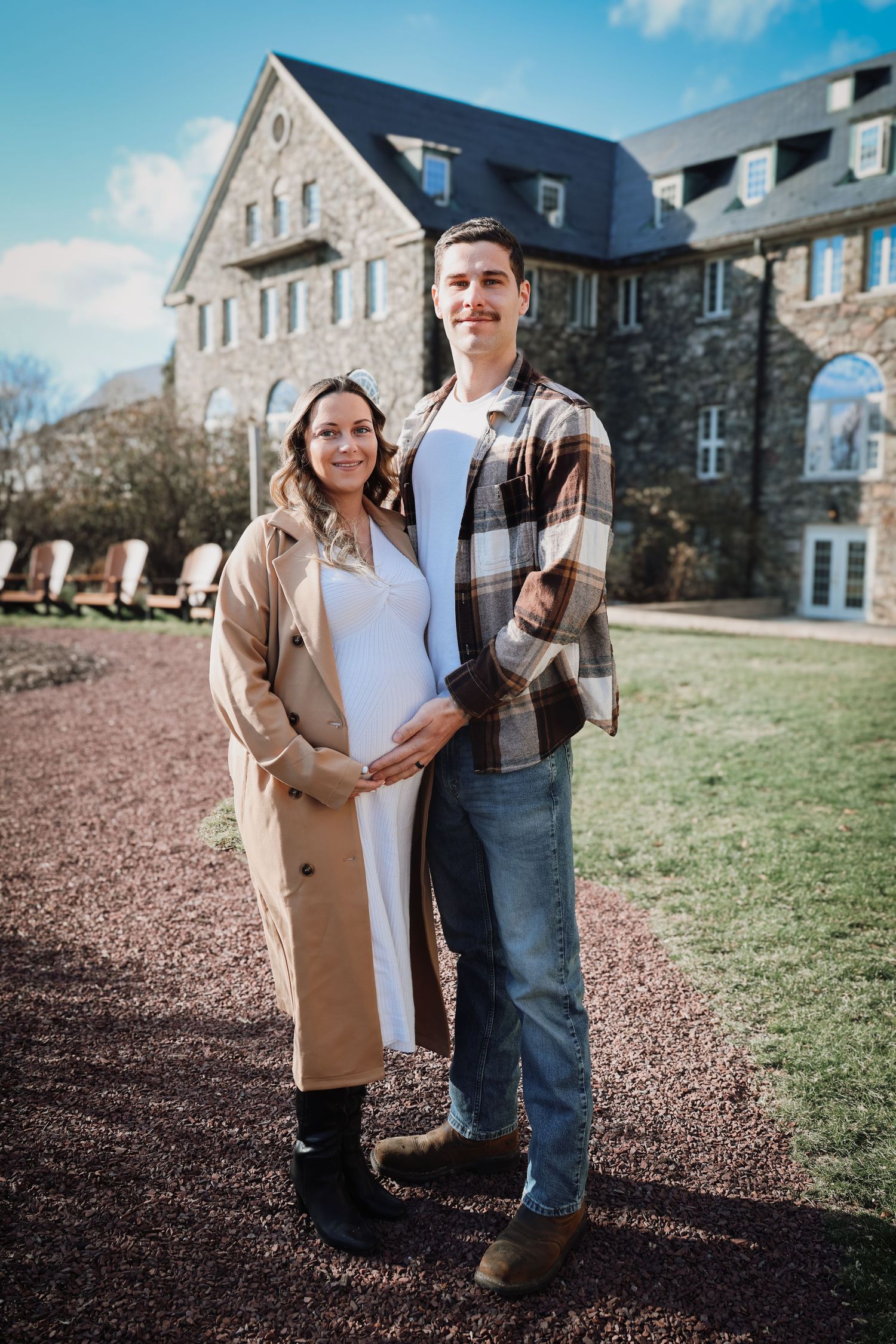 A couple poses together on a path outside a grand stone building on a sunny day.