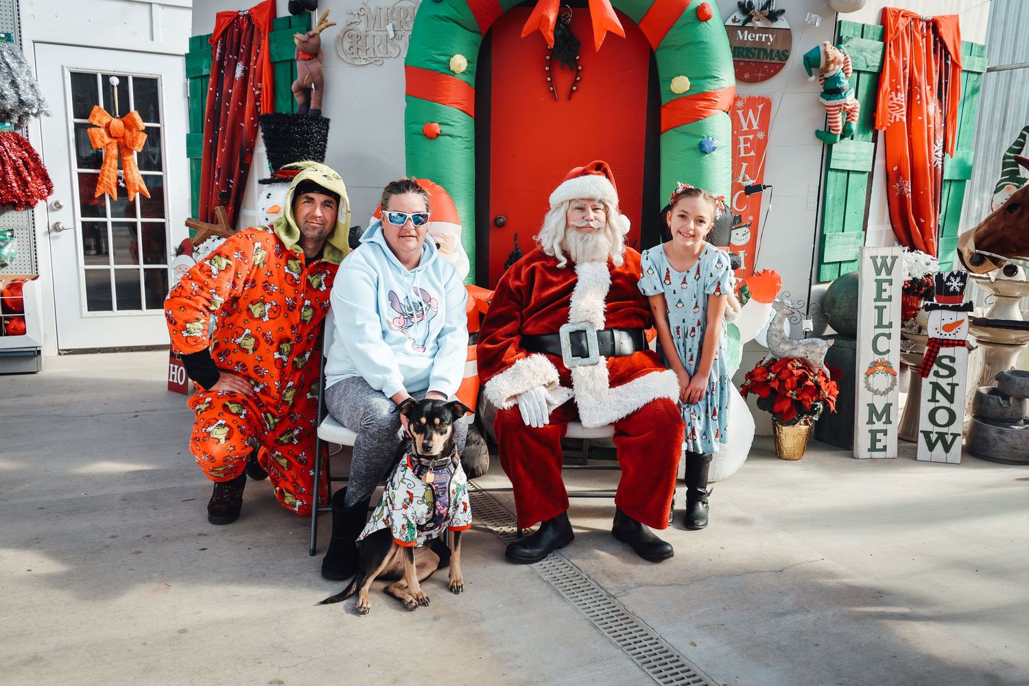 A festive holiday scene with Santa Claus and helpers greeting visitors at a decorated shopping center entrance.
