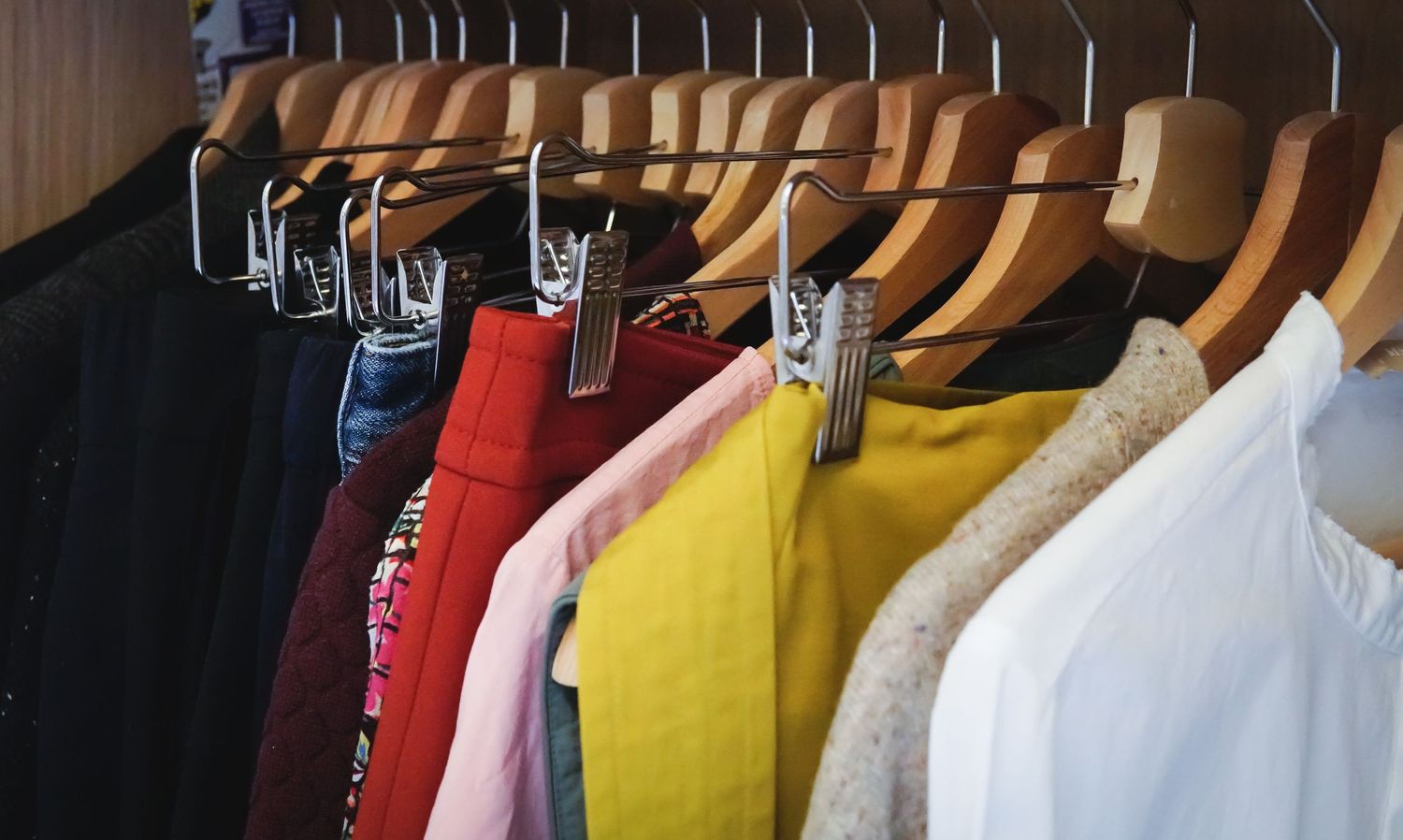 Colorful clothing hanging on wooden hangers in a closet showing various shirts and garments.