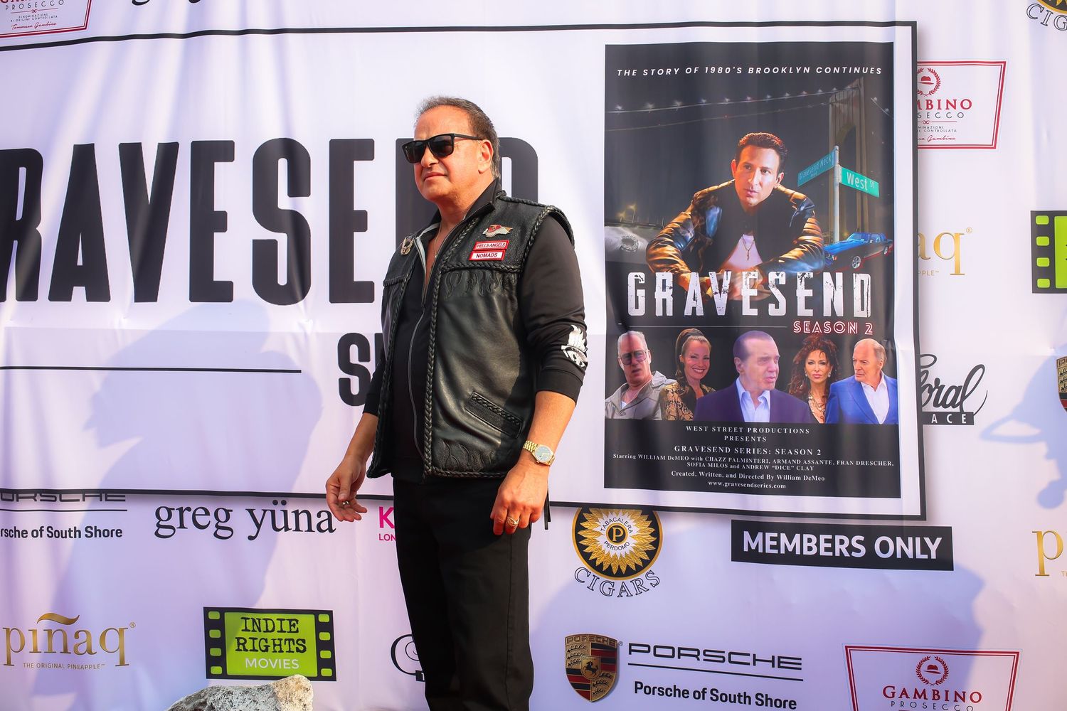 Person wearing sunglasses and dark clothing stands in front of wall covered with promotional posters and banners.