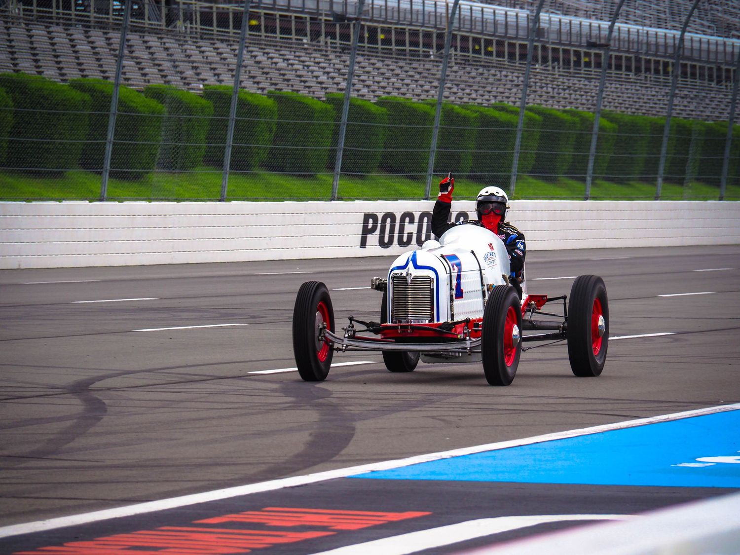 Race car drives on track with tire marks visible on asphalt and blue and red painted racing lines.
