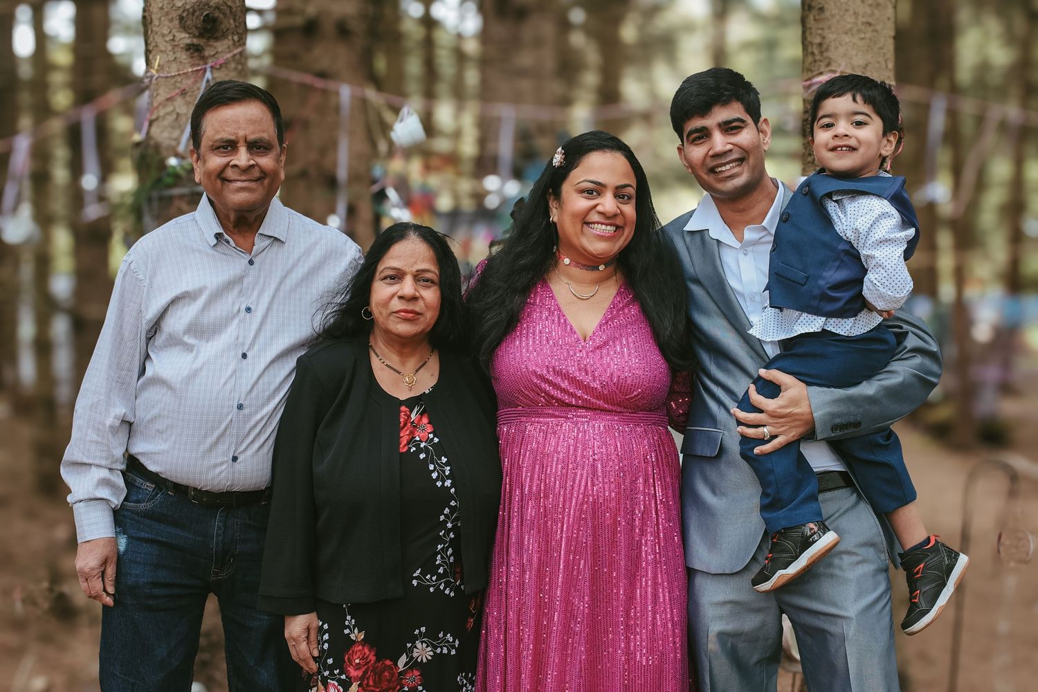 A group of people pose together outdoors in a forest setting wearing formal attire.