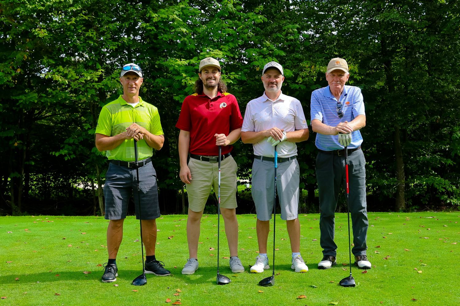 Golfers lined up on a lush green course preparing to take their shots on a sunny day.